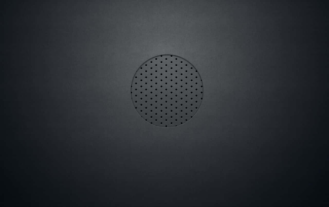 Grunge Texture 桌布 壁紙 — 一個極簡風格的深灰色圓形揚聲器格柵，置於帶有柔和漸變燈光的細微紋理牆壁中央。