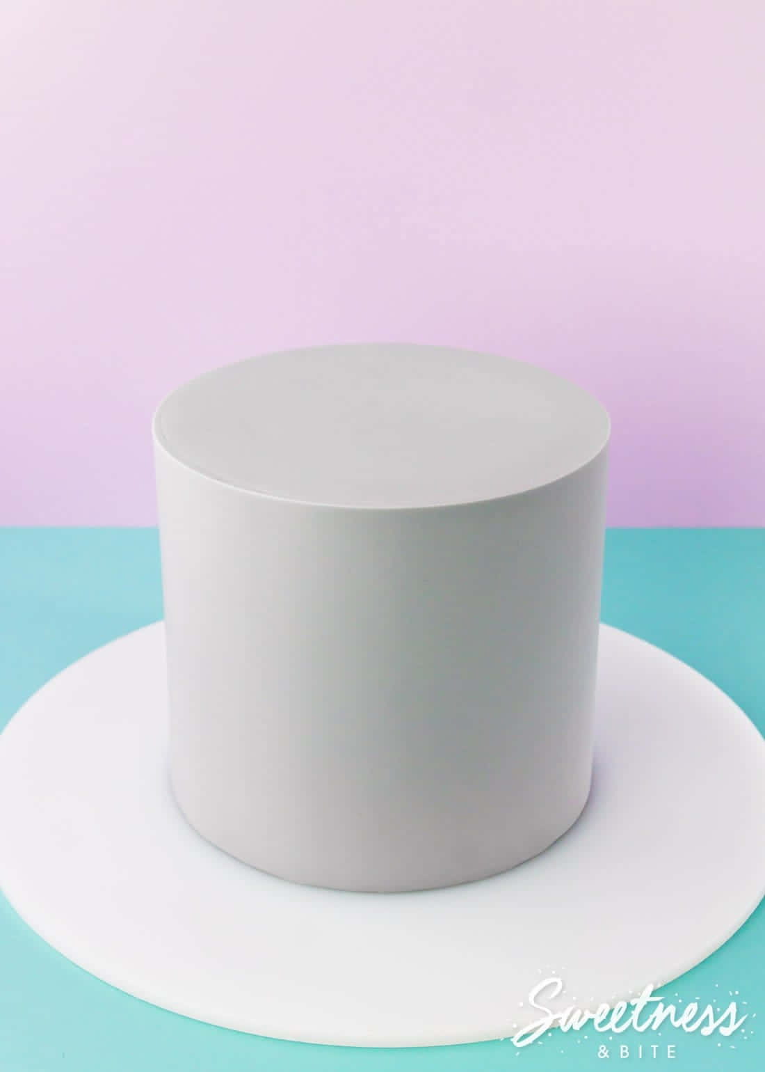 Cake Fondant 桌布 壁紙 — 一個極簡風格的白色圓柱形蛋糕，置於白色盤子中央，背景為柔和的粉紅色和藍綠色。
