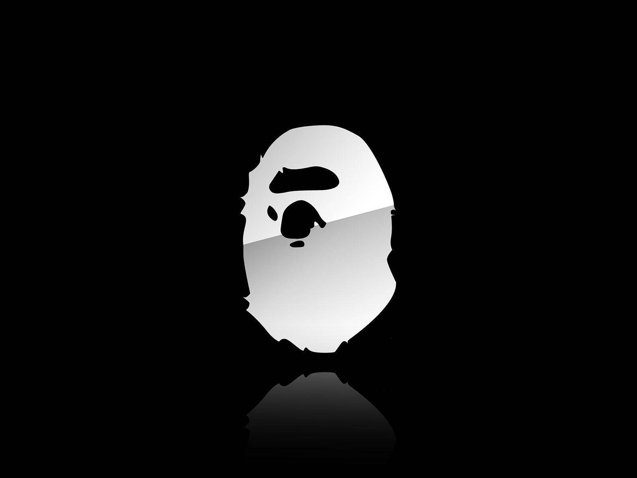 bape logo 桌布 壁紙 — 一個極簡風格的白色猿頭標誌，帶有黑色面部特徵，居中放置在黑色背景上，帶有微妙的倒影。
