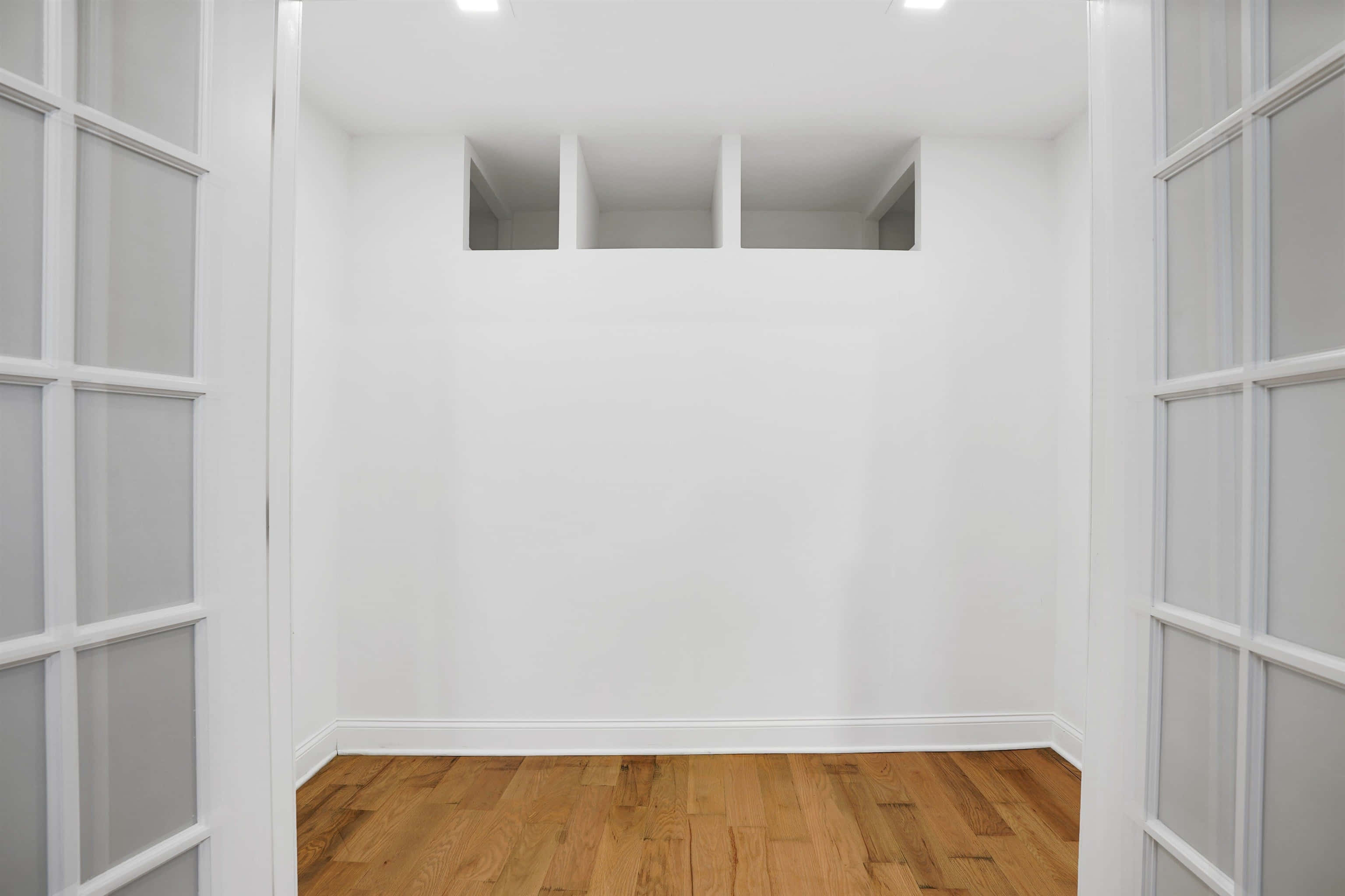 Empty Room 桌布 壁紙 — 一個極簡風格的空房間，有白色牆壁、木地板和磨砂玻璃門，在明亮的頂燈下。