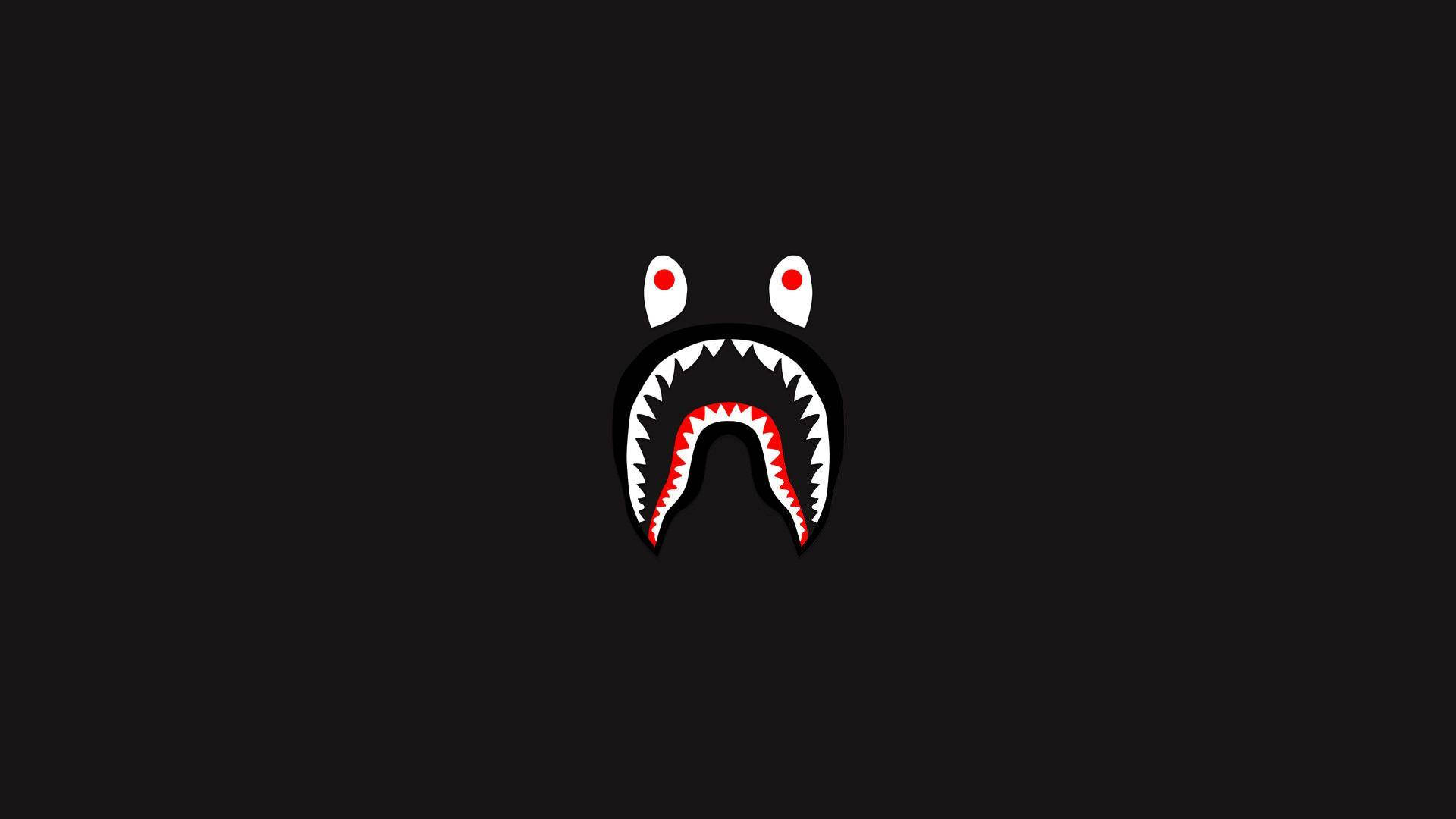 bape logo 桌布 壁紙 — 一個極簡風格的鯊魚臉，紅眼睛和尖牙，從黑色背景中凝視。