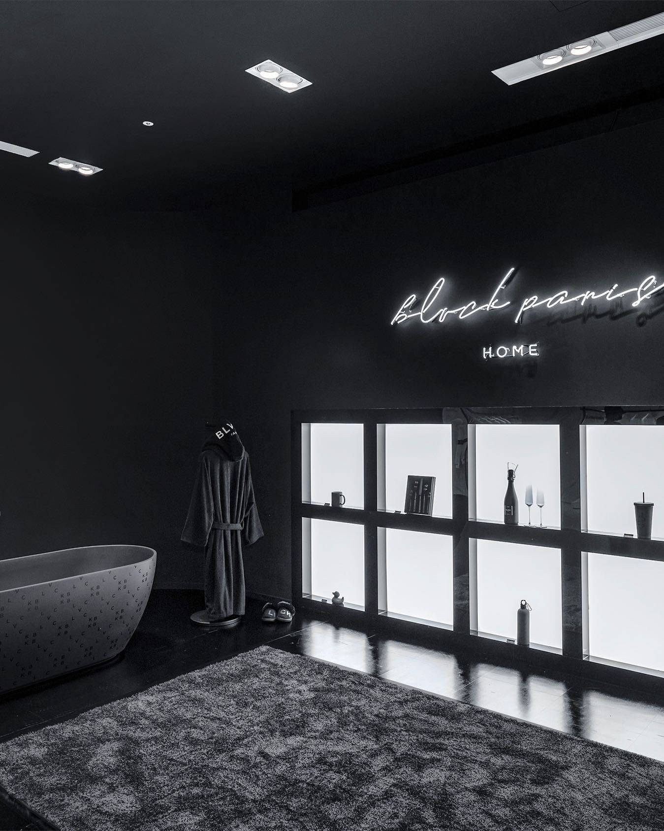 Blvck Paris 桌布 壁紙 — 一個極簡風格的黑色浴室，配有獨立式浴缸、發光霓虹燈標誌和帶照明的層架單元。