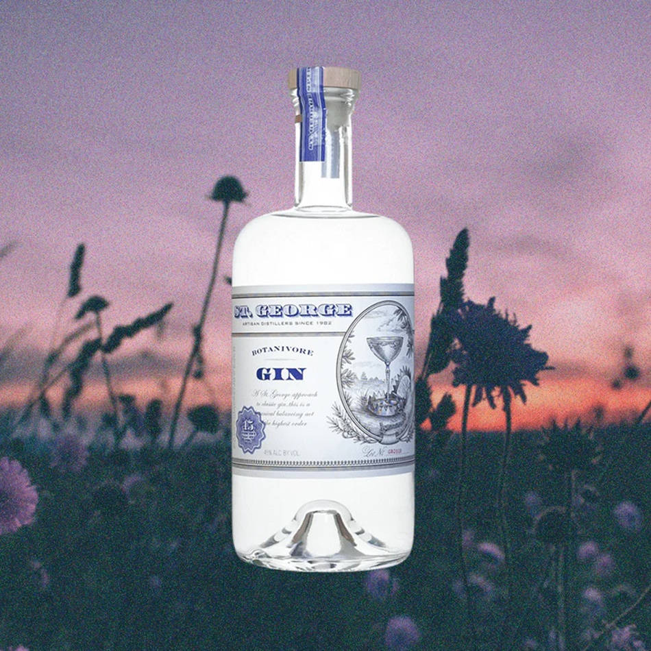 Drink 桌布 壁紙 — 一個標有 St George Botanivore 的透明琴酒瓶矗立在紫色野花田中，背景是粉紅和橙色的日落天空。