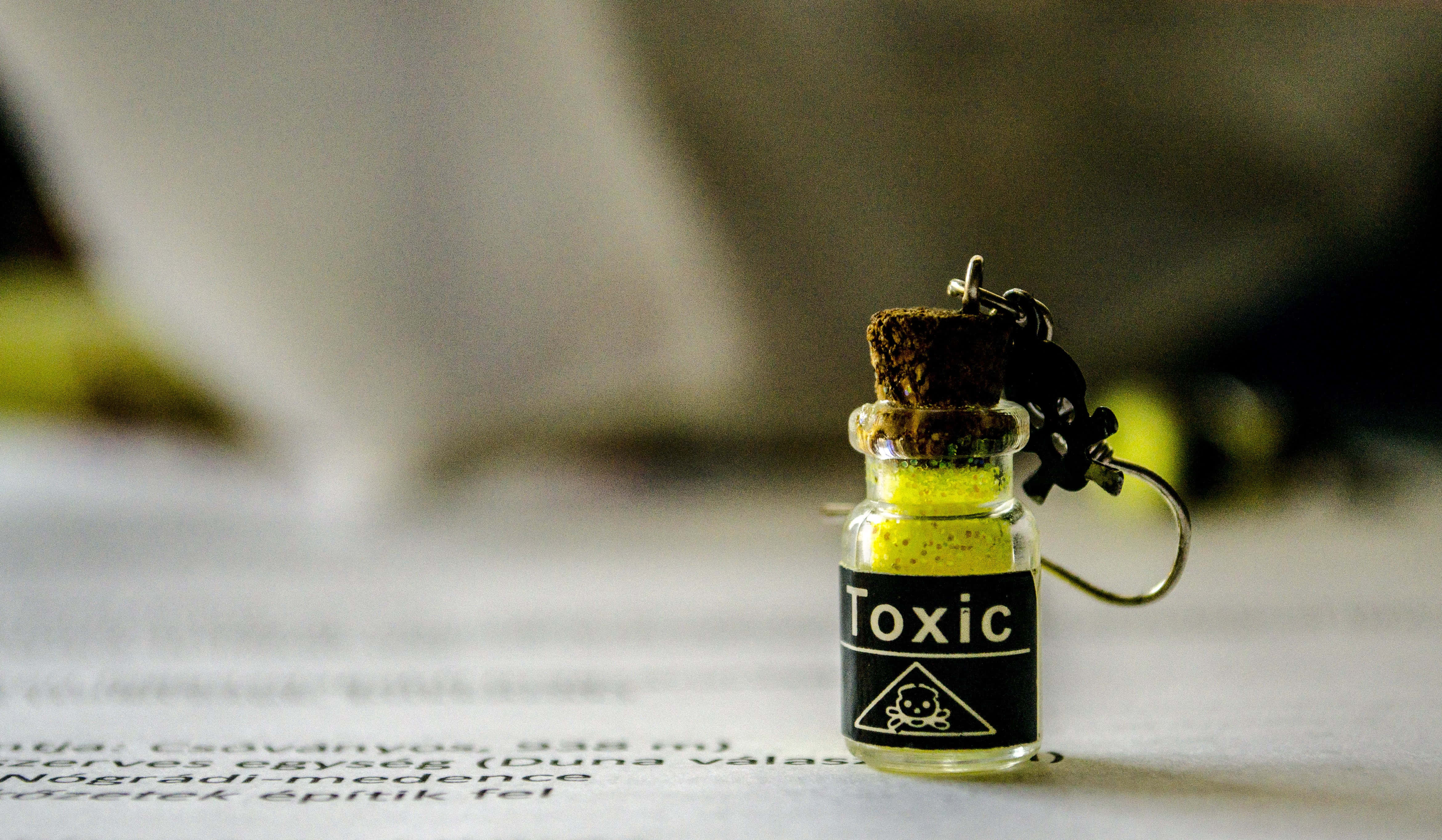 toxic 桌布 壁紙 — 一個標有有毒的細小玻璃小瓶，裝有黃色粉末，放在一份背景模糊的文件上。