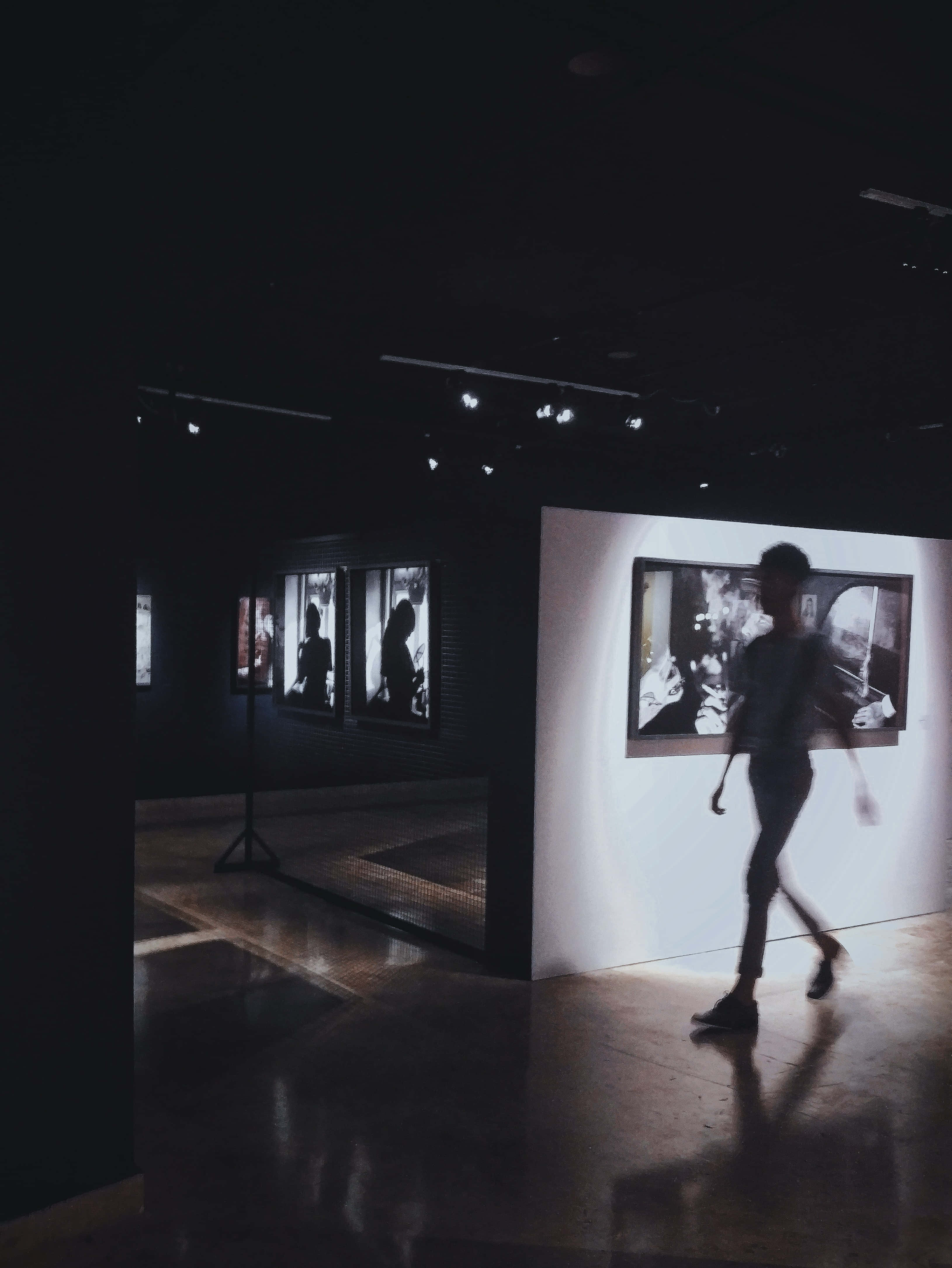 Gallery 桌布 壁紙 — 一個模糊的人影穿過一個燈光昏暗的藝術畫廊，牆上掛著裱框的黑白照片。
