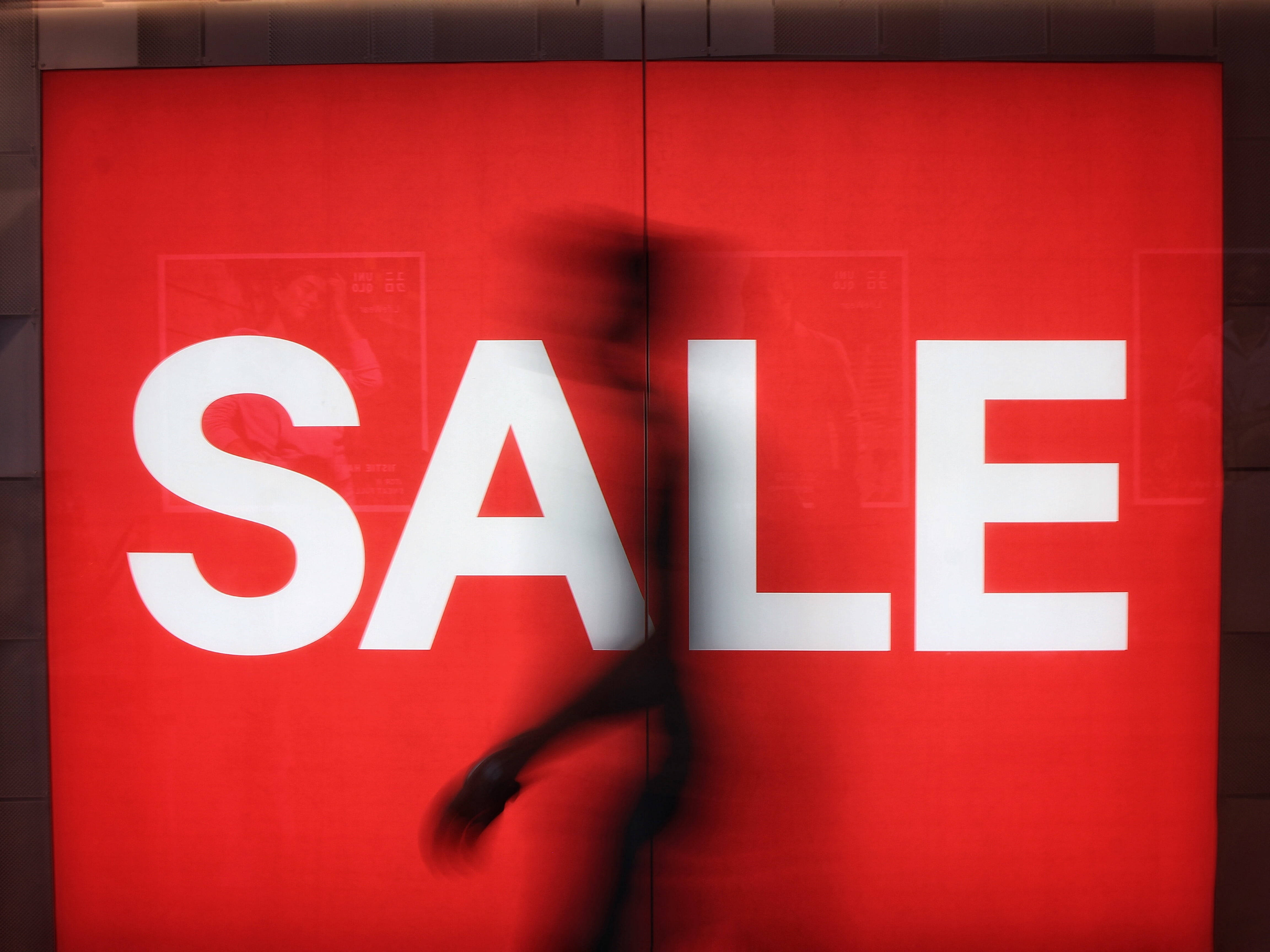 Sales 桌布 壁紙 — 一個模糊的人影走過一個鮮紅色、帶有粗體白色字體的減價標誌。