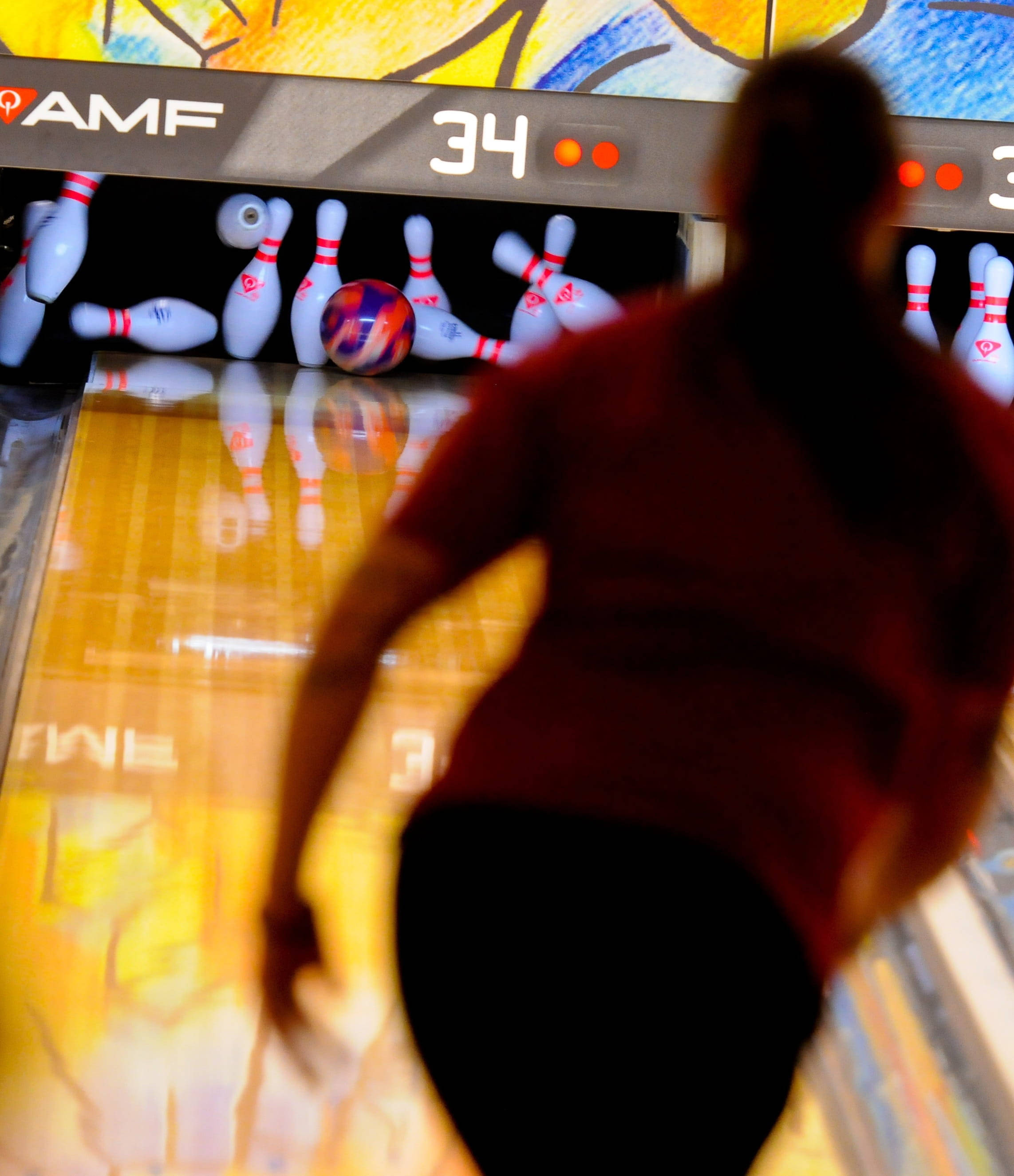 Bowling 桌布 壁紙 — 一個模糊的保齡球手在移動中，在明亮的AMF球道燈光下向倒下的球瓶釋放一個色彩繽紛的球。