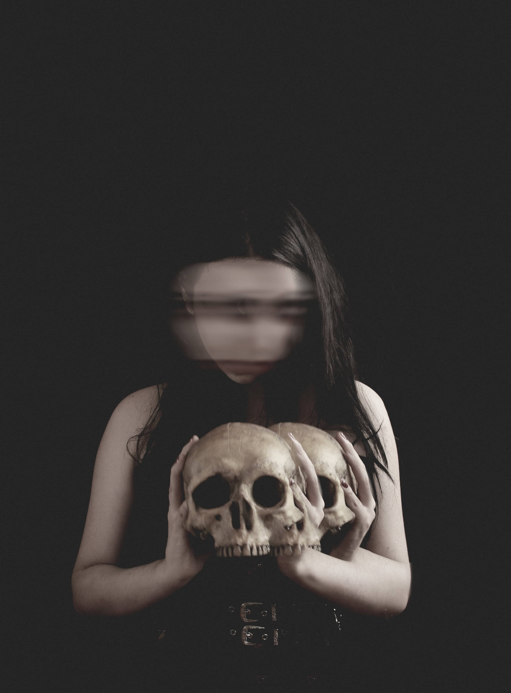 Goth 桌布 壁紙 — 一個模糊的身影，長長的黑髮，在漆黑的背景下，拿著兩個頭骨，構成一幅令人難忘的肖像。