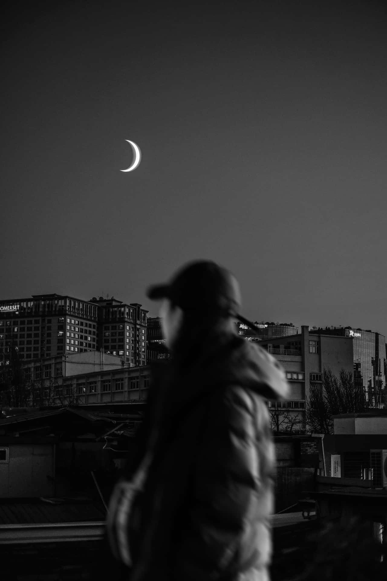 高清 桌布 壁紙 — 一個模糊的身影在夜晚的都市景觀中，於新月下以單色走過。