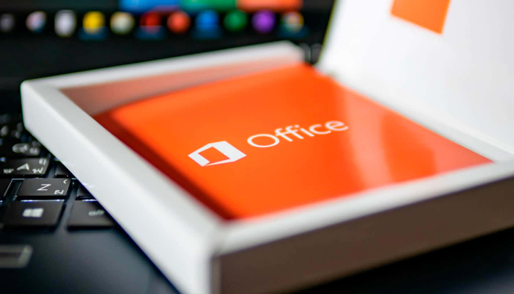 Office 365 桌布 壁紙 — 一個橙色Microsoft Office盒的特寫，放在筆記型電腦鍵盤上，背景有模糊的彩色圖示。