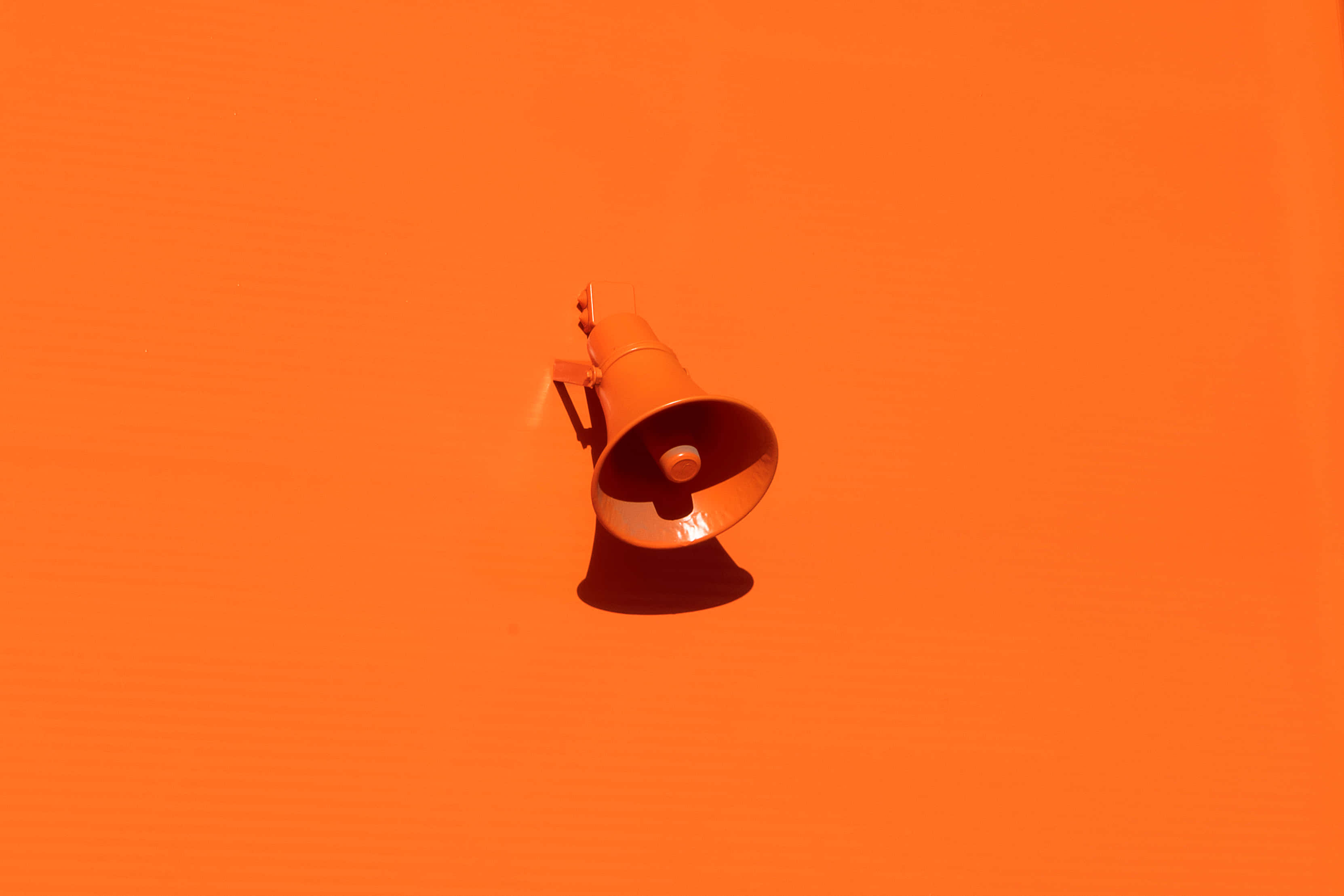 Orange Desktop 桌布 壁紙 — 一個橙色擴音器在純橙色背景上投射出銳利陰影，構成極簡構圖。