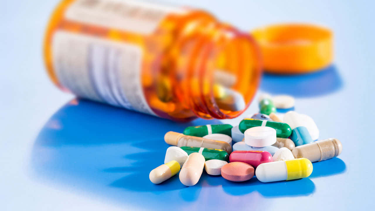 pills 桌布 壁紙 — 一個橙色藥瓶打翻，各種彩色藥丸散落在亮藍色表面上。