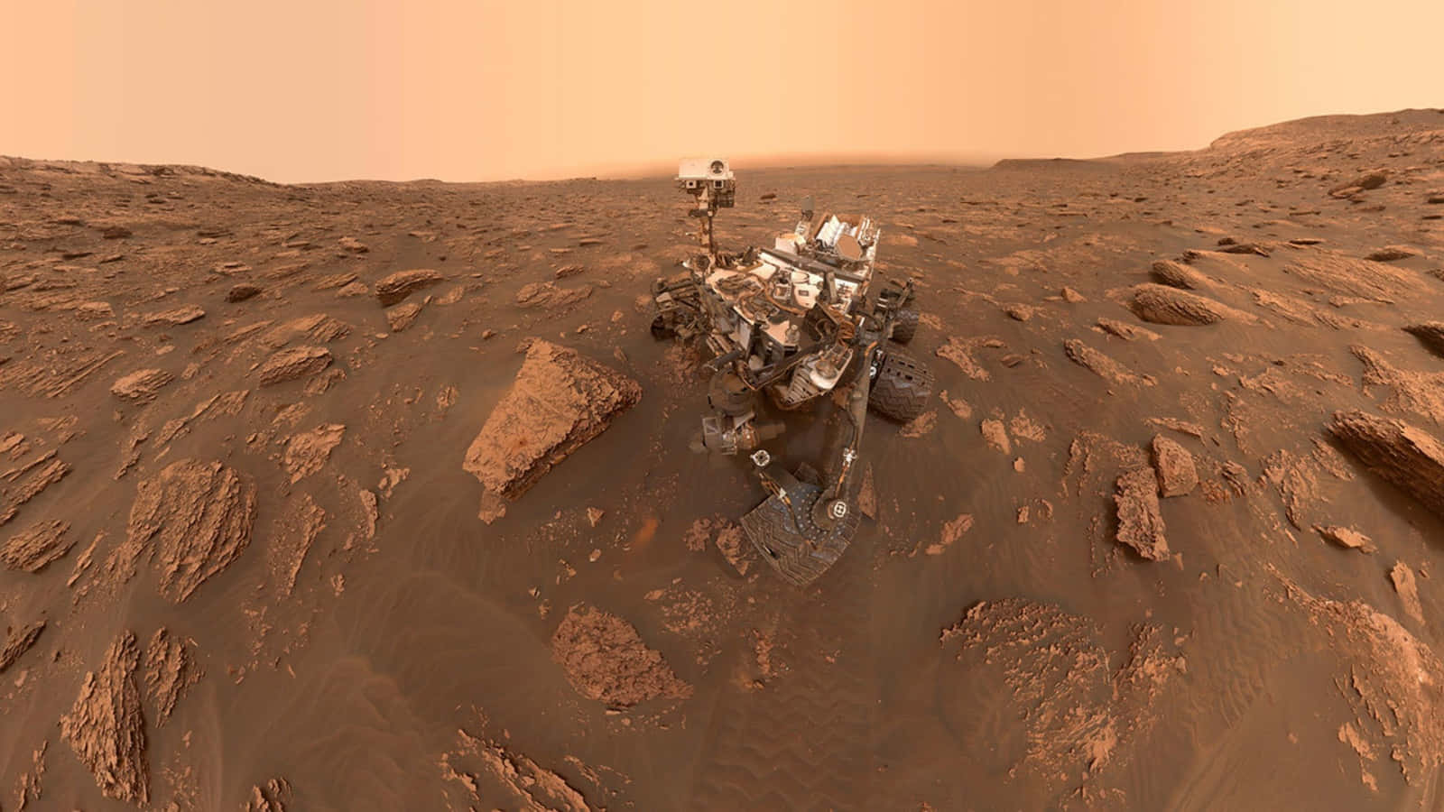 NASA 動態圖片 桌布 壁紙 — 一個機器人探測車站在岩石火星表面，在朦朧的橙色天空下，散落著巨石。