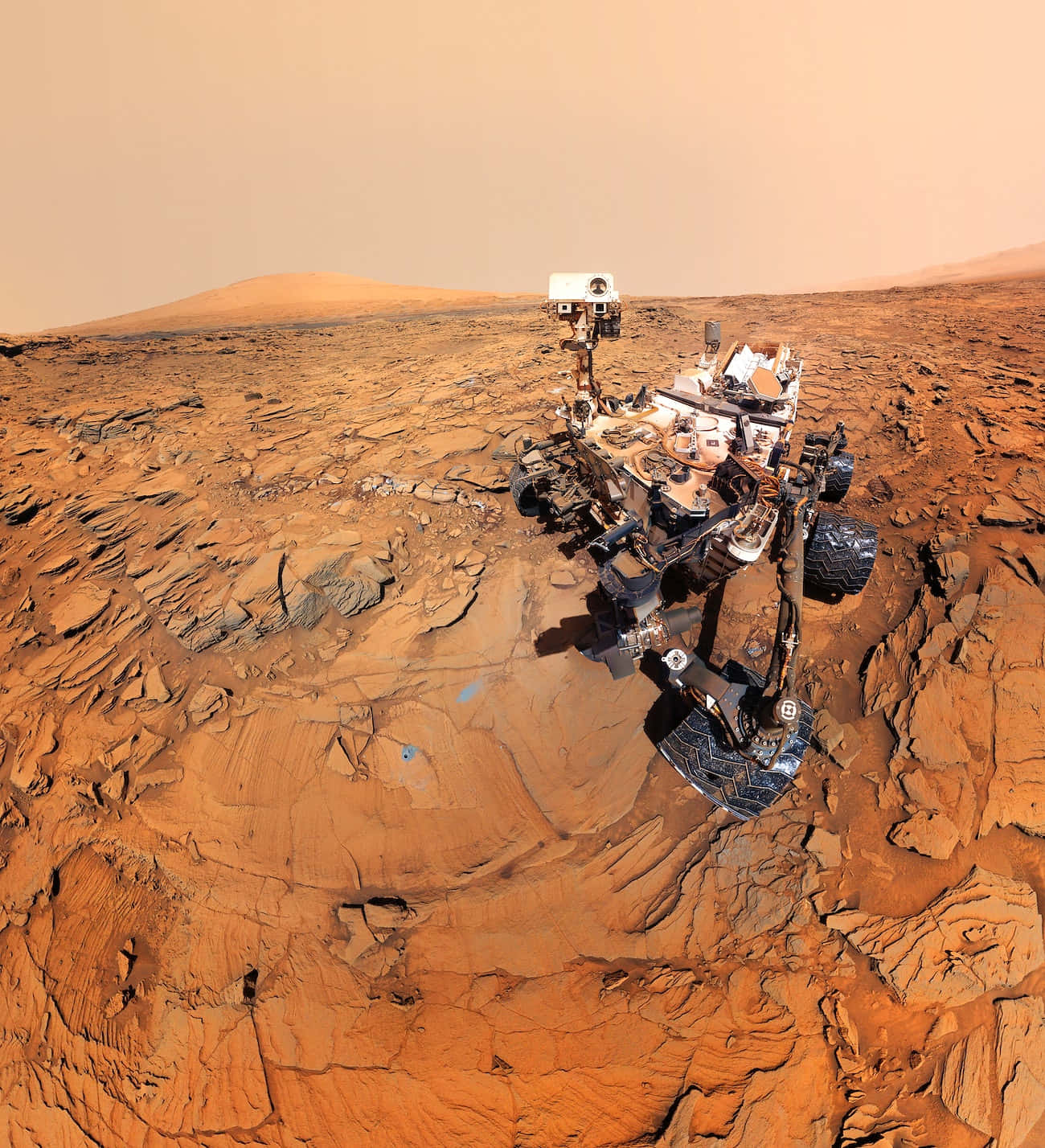 NASA 動態圖片 桌布 壁紙 — 一個機器人探測車站在火星鏽紅色的表面上，周圍是裂開的地形，天空是朦朧的橙色。