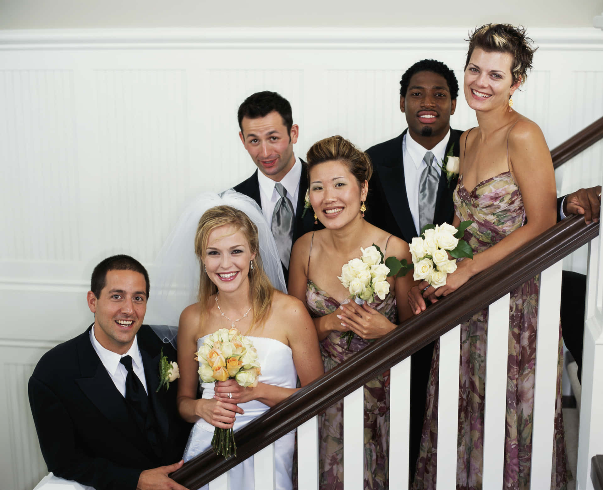Bridal 桌布 壁紙 — 一個歡樂的婚禮派對在帶有深色木扶手的白色樓梯上擺姿勢，穿著正式服裝燦爛微笑。