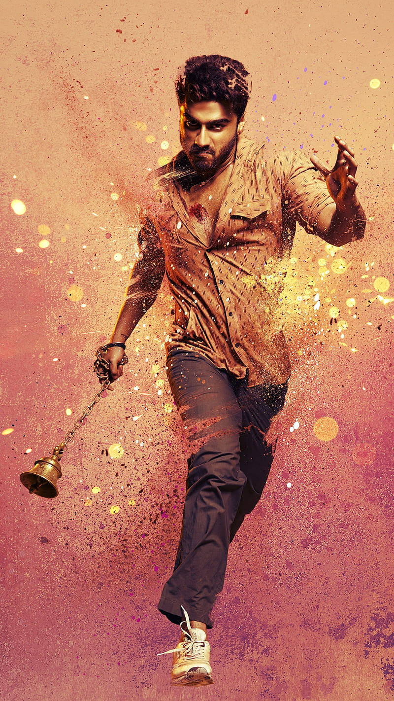 Arjun Kapoor 桌布 壁紙 — 一個正在移動的男人拿著一個鈴鐺，色彩繽紛的油漆飛濺在他周圍爆炸，背景是溫暖的漸變色。