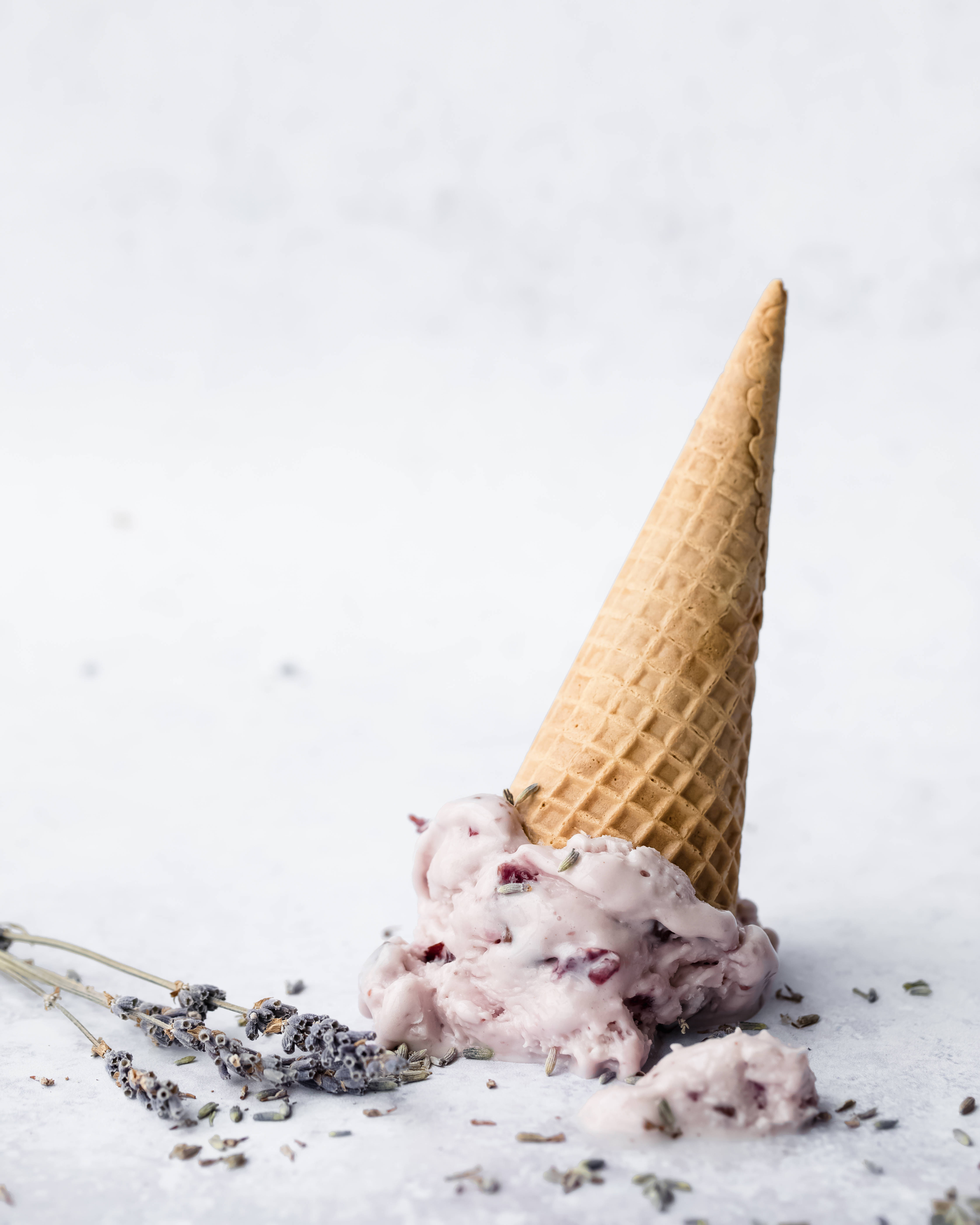 Ice Cream 桌布 壁紙 — 一個正在融化的薰衣草冰淇淋甜筒，淺灰色表面上散落著乾燥的薰衣草花蕾。