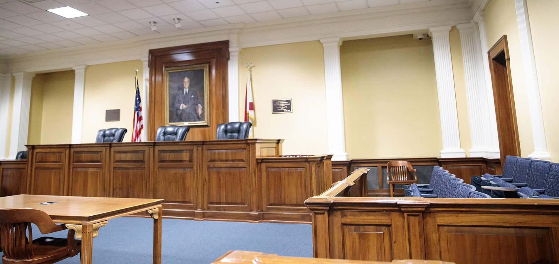 Courtroom 桌布 壁紙 — 一個正式的法庭，設有木製長椅、藍色地毯和法官席，上方掛著一幅男子肖像。