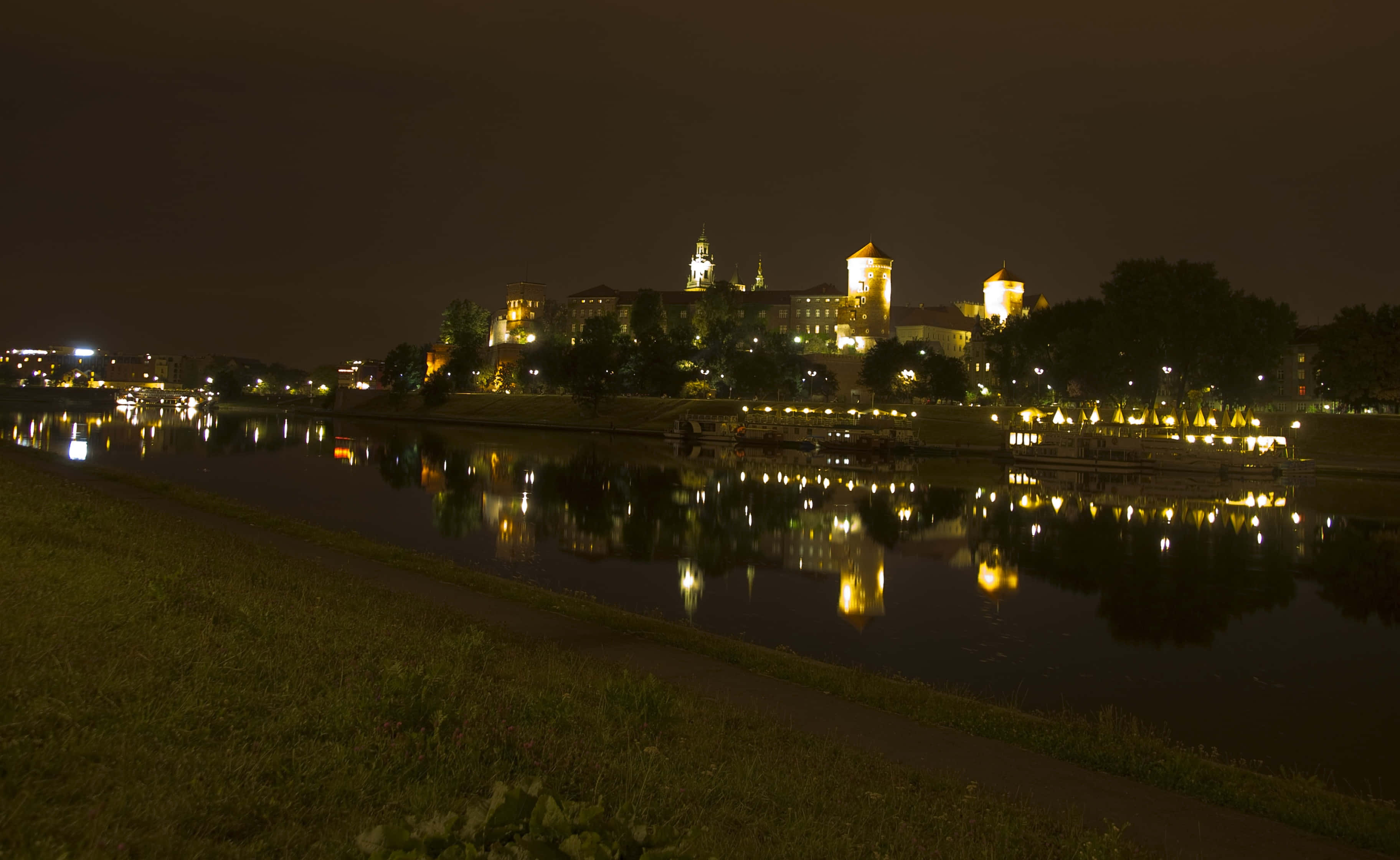 night night 桌布 壁紙 — 一個歷史悠久的城堡建築群在夜晚溫暖地發光，其燈光完美地倒映在下方平靜的河流中。