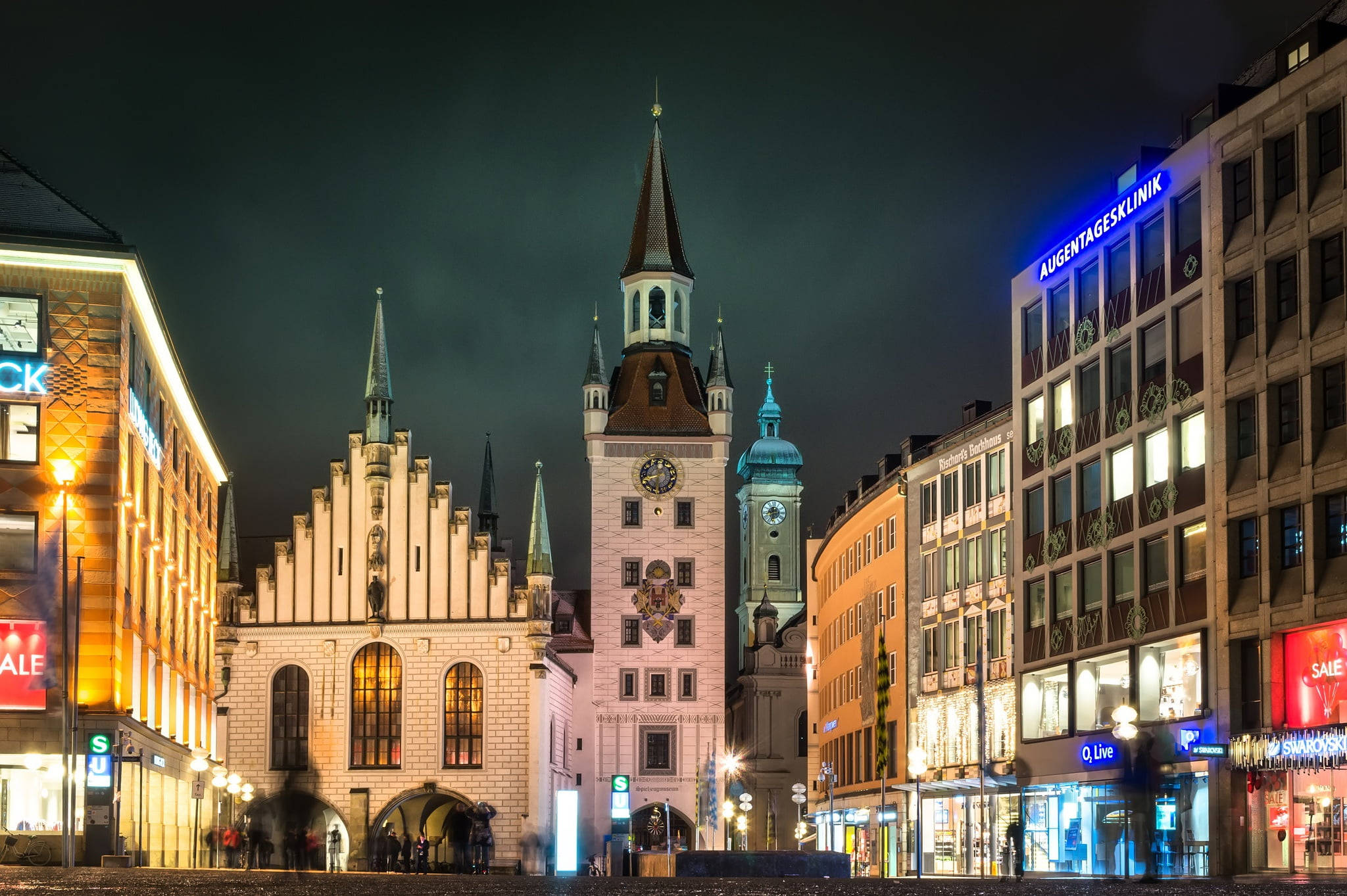 Munich 桌布 壁紙 — 一個歷史悠久的歐洲城鎮廣場的充滿活力的夜景，被溫暖的路燈和發光的商店櫥窗照亮。