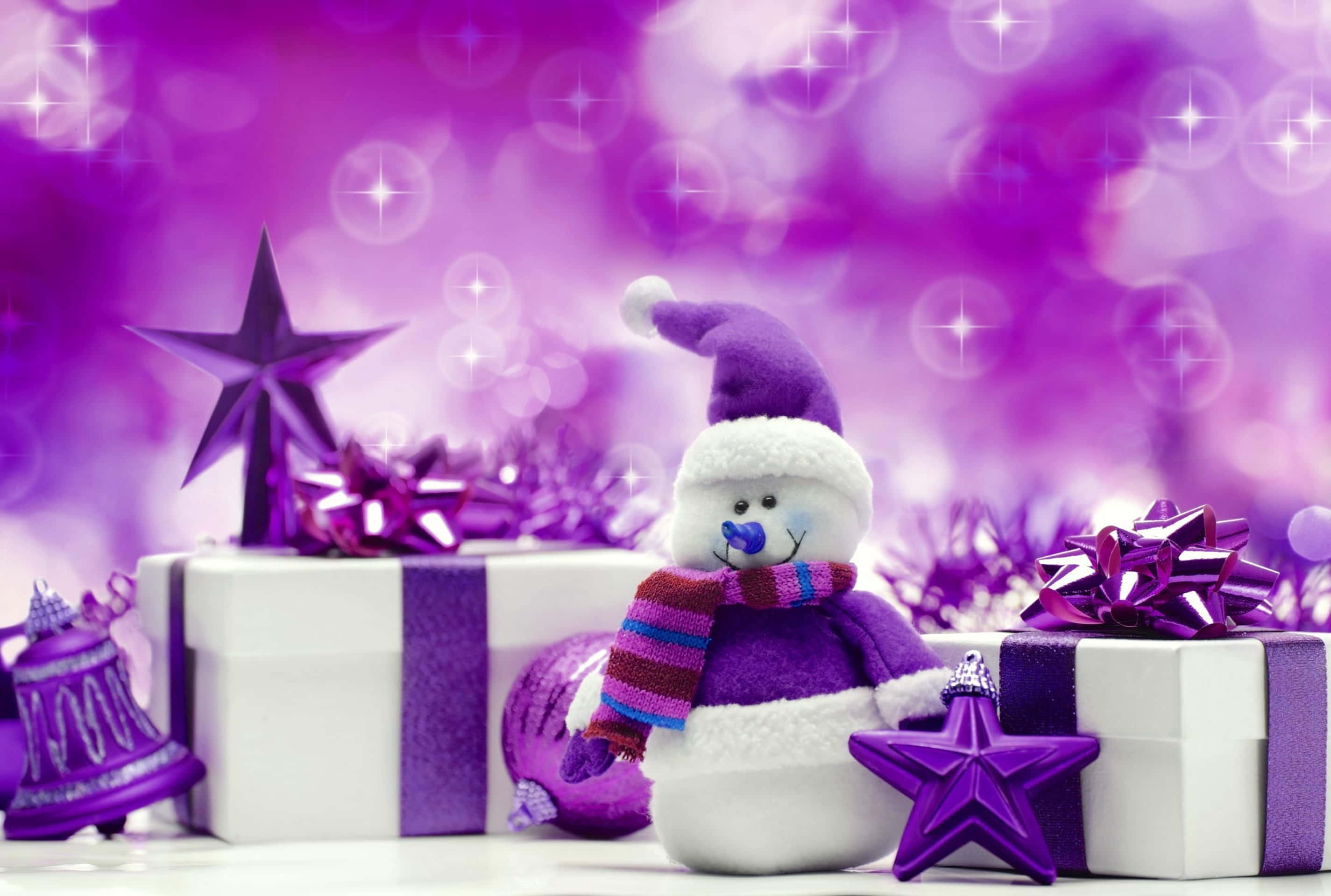 Purple Christmas 桌布 壁紙 — 一個毛絨絨的雪人戴著紫色帽子和圍巾，坐在白色禮物盒和紫色裝飾品旁邊，背景是閃爍的紫色散景。