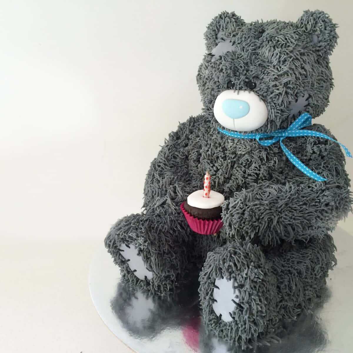Teddy Bear 桌布 壁紙 — 一個毛茸茸的灰色泰迪熊蛋糕拿著一個插著一支蠟燭的杯子蛋糕，放在銀色托盤上，背景是純白色。