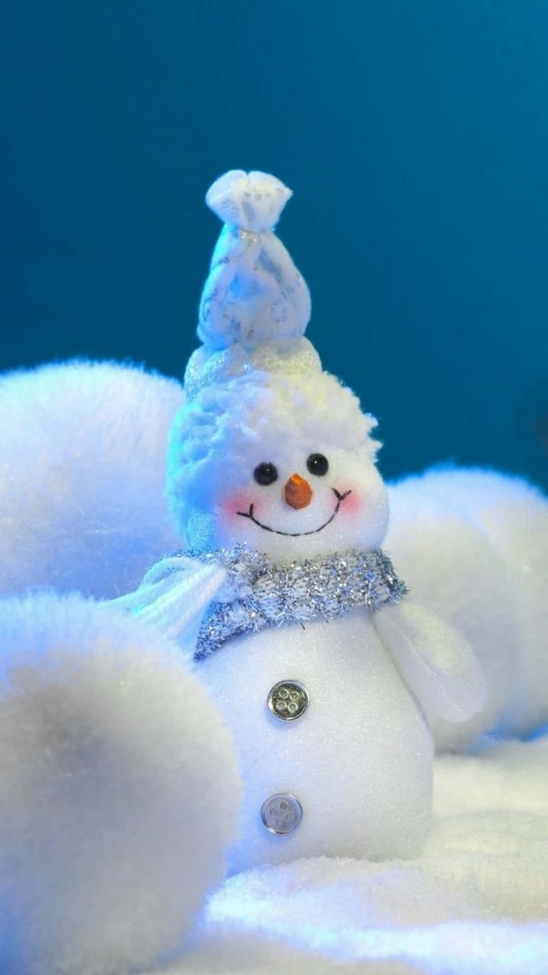 一個毛茸茸的雪人玩具，戴著閃閃發光的圍巾和胡蘿蔔鼻子，在藍光中微笑。 — 雪人 壁紙