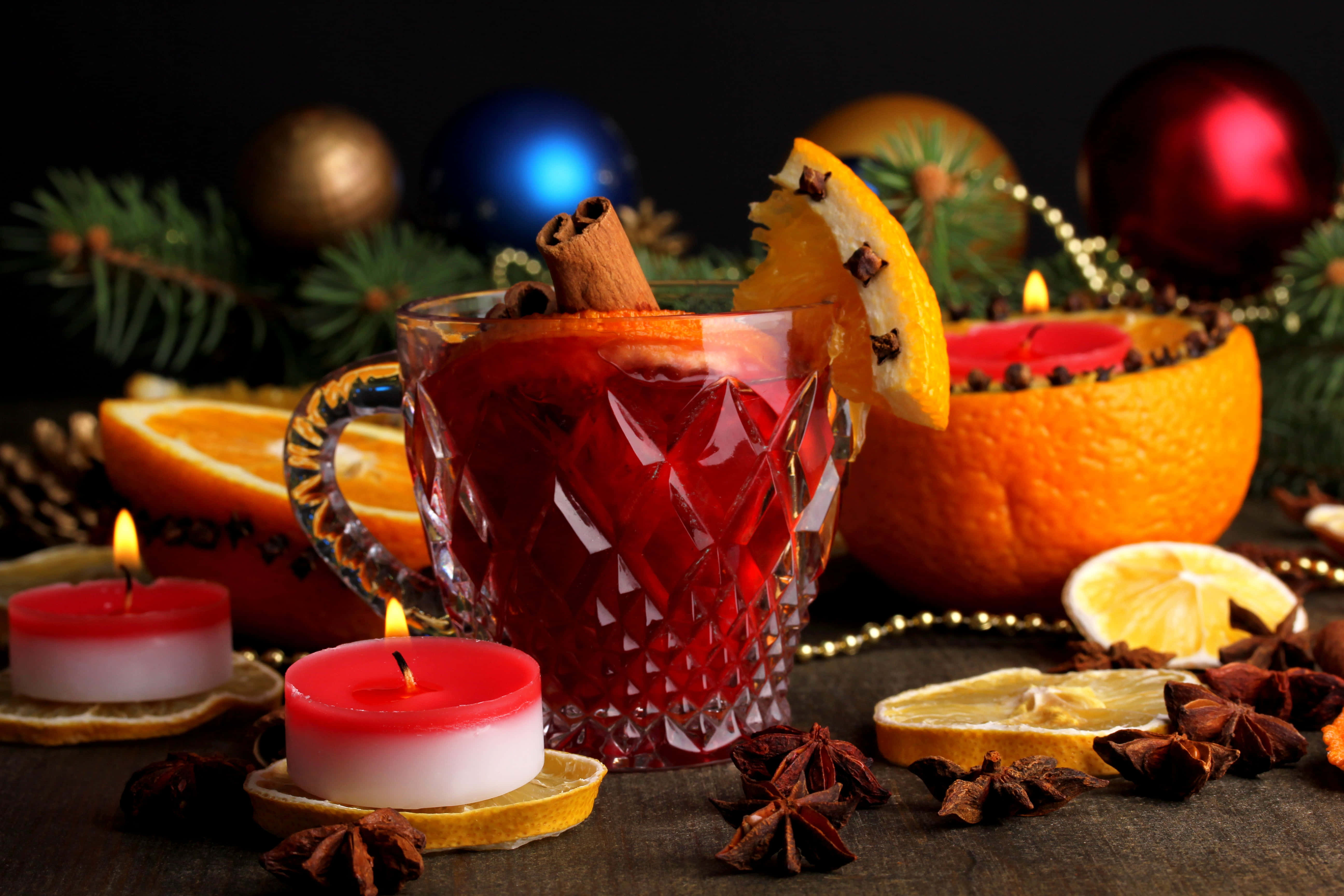 Mulled Wine 桌布 壁紙 — 一個水晶杯盛載著香料紅酒，飾以柳橙和肉桂棒，旁邊放著點燃的蠟燭和節慶聖誕裝飾。