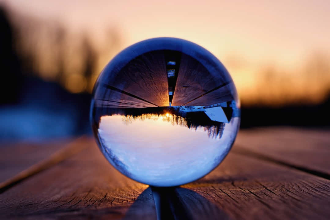 reflection 桌布 壁紙 — 一個水晶球放在木頭上，反射出水面上的鮮豔日落和樹木剪影。