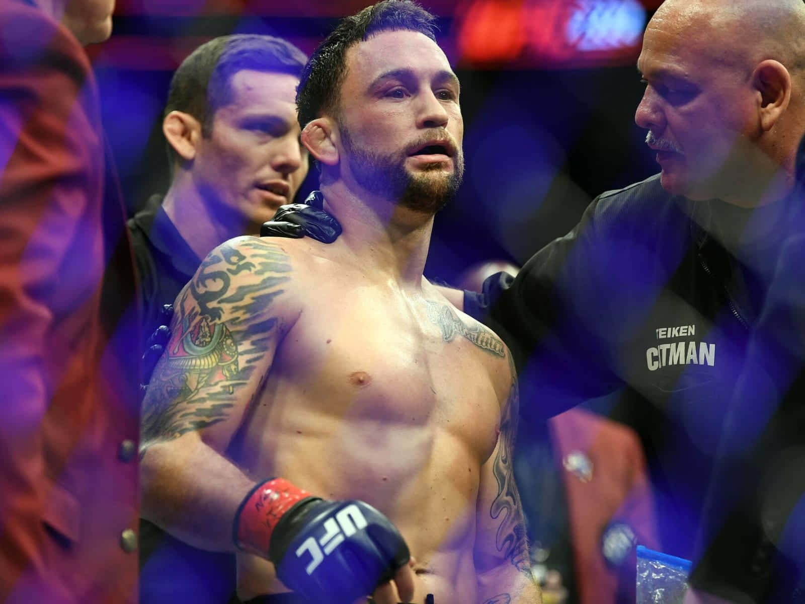 UFC 桌布 壁紙 — 一個汗流浹背、有刺青的拳手戴著UFC手套站在擂台上，裁判在明亮的場館燈光下檢查他。