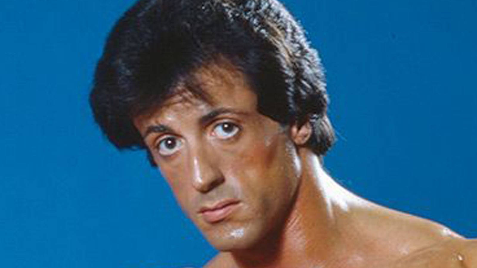 rocky 桌布 壁紙 — 一個汗流浹背、沒穿衣服的深色頭髮男人，在純藍色背景前強烈凝視。