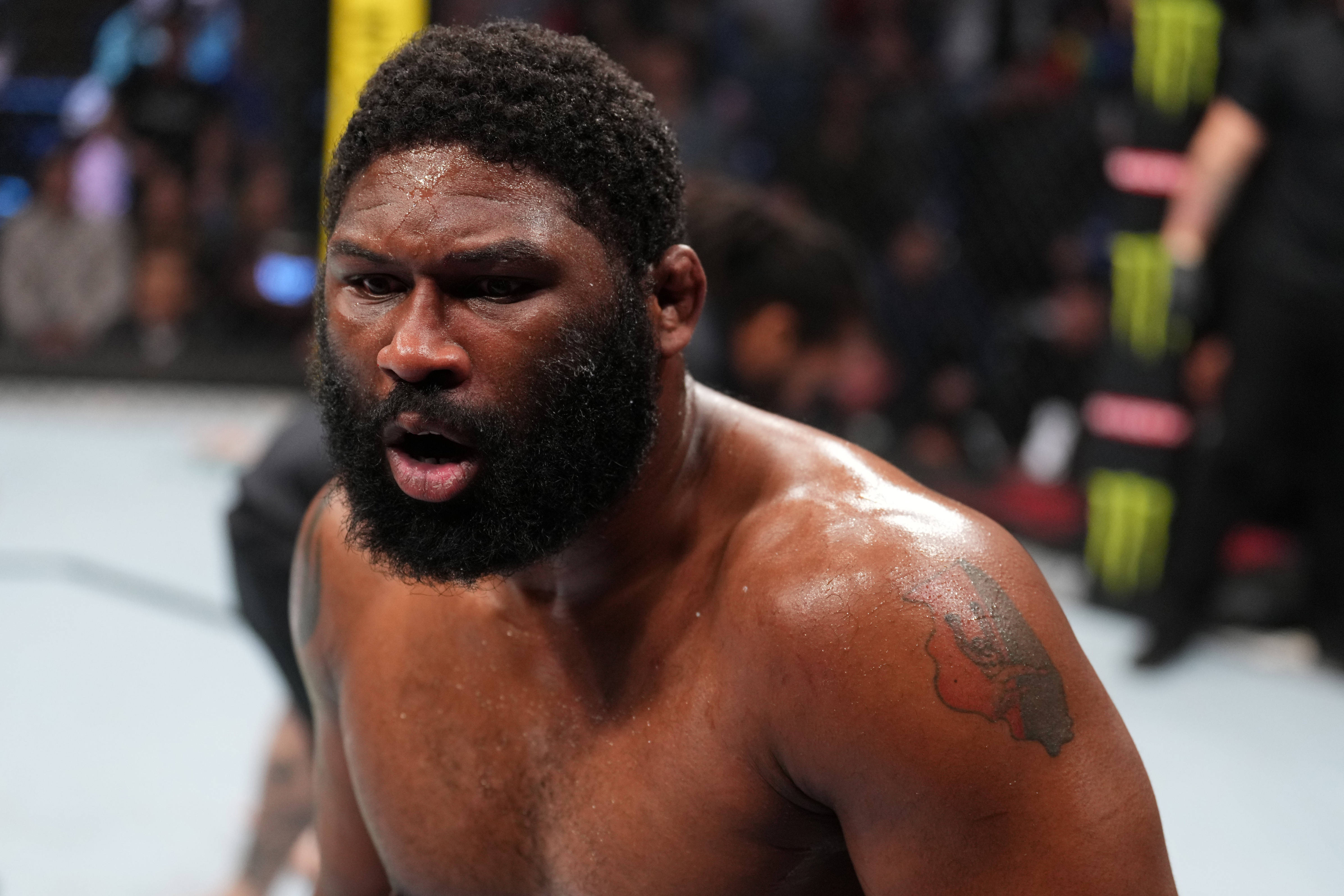 UFC 桌布 壁紙 — 一個汗流浹背、留鬍子的拳手在燈光明亮的八角籠中進行綜合格鬥比賽時，表情痛苦地扭曲。