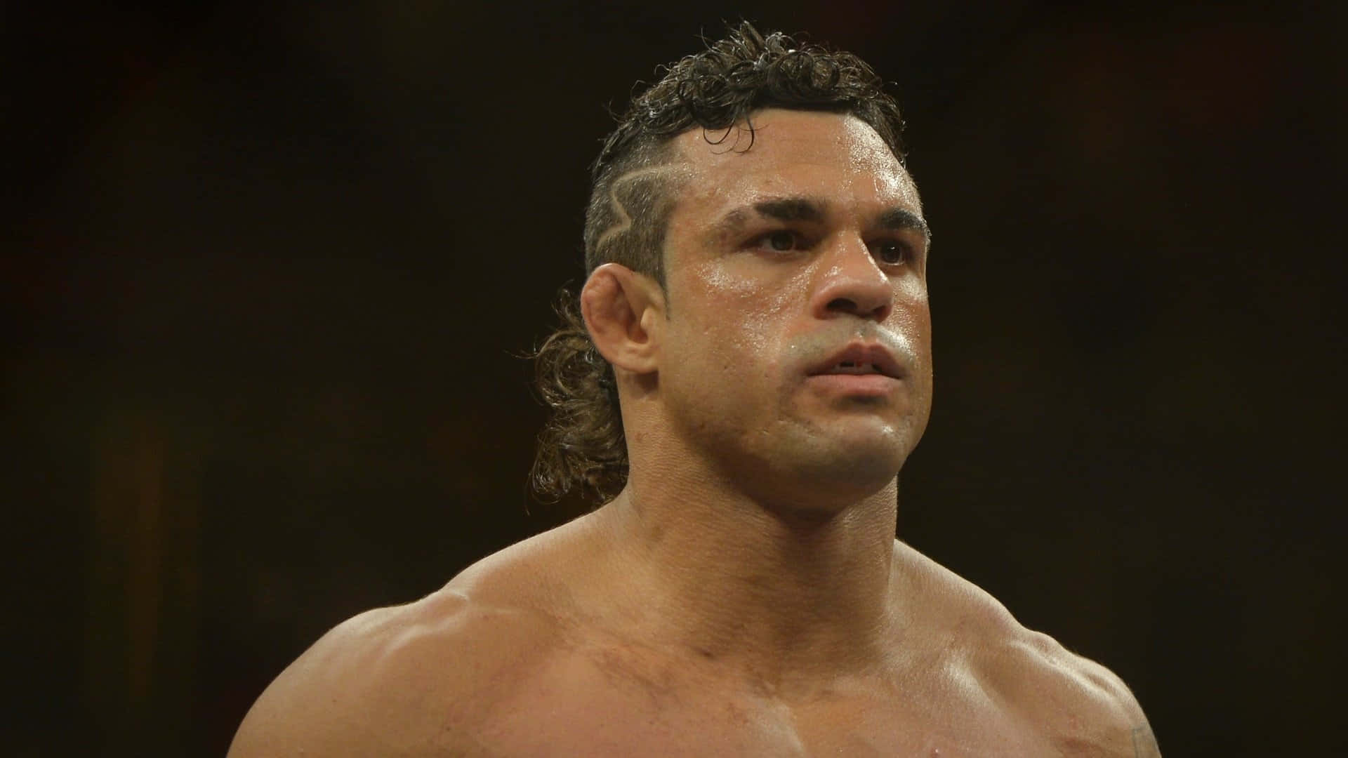 UFC 桌布 壁紙 — 一個汗流浹背、肌肉發達的戰士，在昏暗的競技場中以銳利的目光直視前方。
