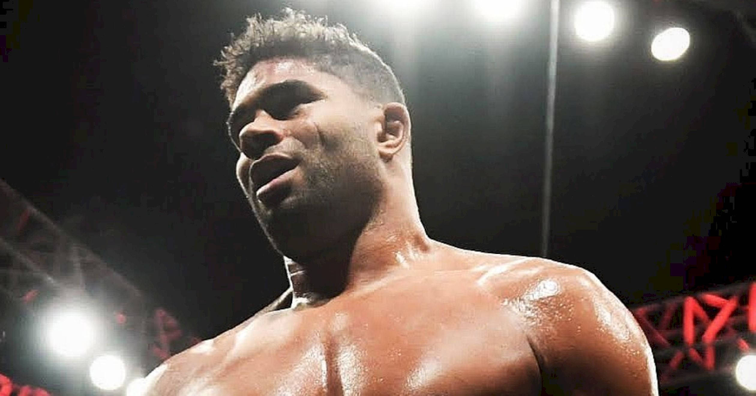 UFC 桌布 壁紙 — 一個汗流浹背、肌肉發達的摔角手在明亮的競技場燈光下，背景有紅色結構橫樑，凝視著前方。