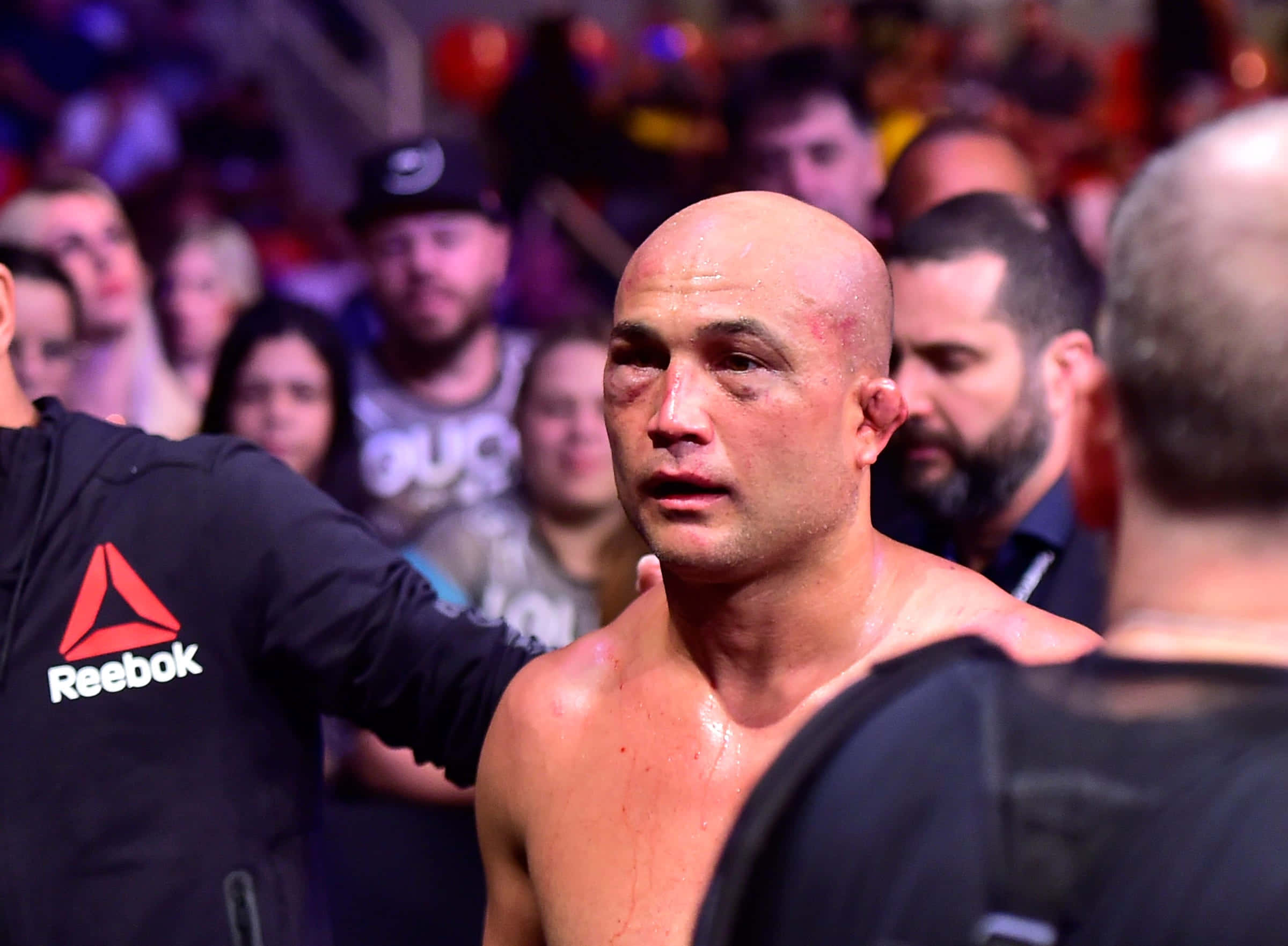 MMA 桌布 壁紙 — 一個汗流浹背的光頭拳手，眼睛瘀傷，站在擠滿觀眾的競技場中，剛經歷了一場殘酷的比賽。