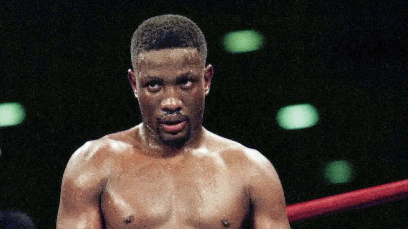 Boxing 桌布 壁紙 — 一個汗流浹背的拳擊手在昏暗的擂台上，背景有發光的綠色燈光，他專注地凝視著。