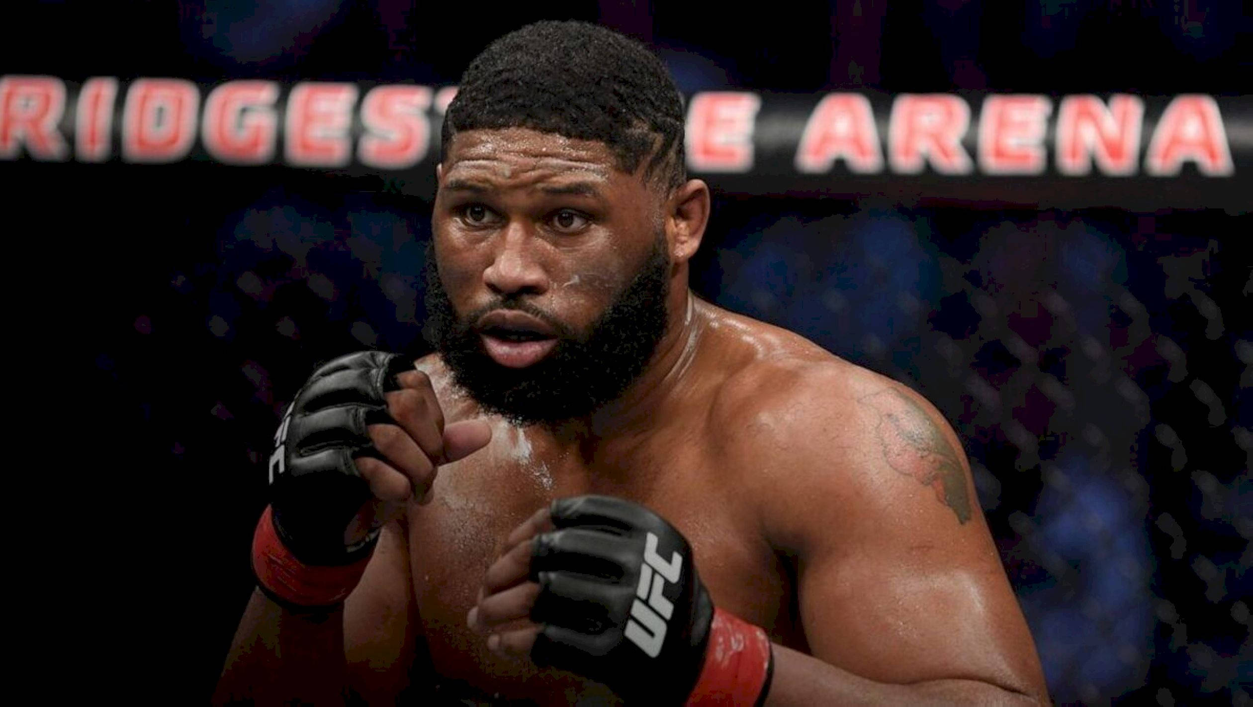 UFC 桌布 壁紙 — 一個汗流浹背的肌肉發達拳手戴著黑色手套，在燈光昏暗的競技場內強烈地指向鏡頭，身後有 'RIDGESTONE ARENA' 標誌。