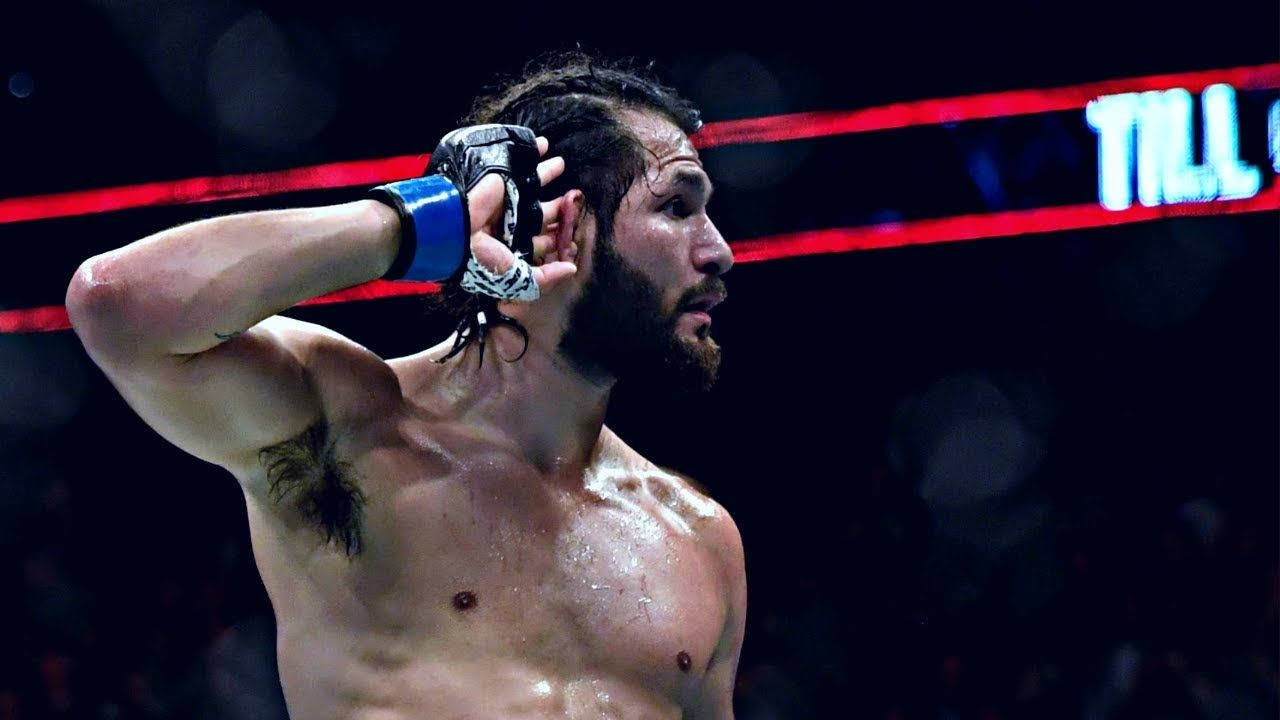 UFC 桌布 壁紙 — 一個汗流浹背的鬍鬚拳擊手在拳擊台上，在明亮的場館燈光下舉起戴手套的手慶祝勝利。