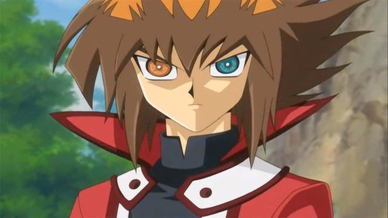 Jaden Yuki 桌布 壁紙 — 一個決心堅定的動畫男孩，擁有異色瞳和刺蝟般的棕色頭髮，穿著紅白相間的服裝，背景是模糊的綠色和岩石。