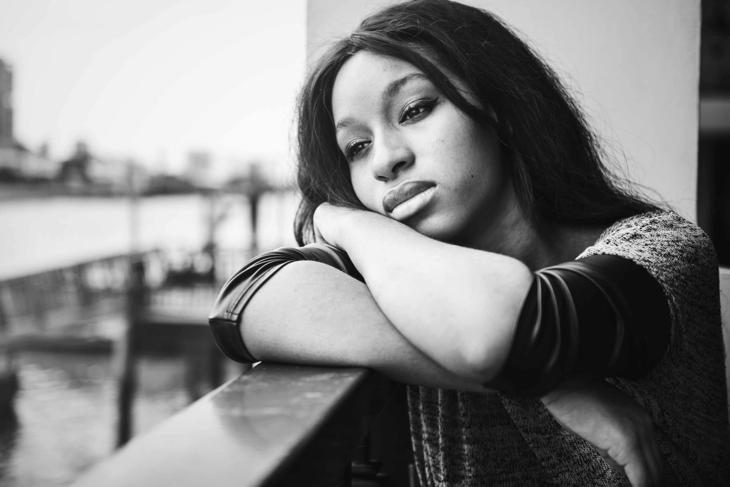 grief 桌布 壁紙 — 一個沉思的女人將下巴擱在手臂上，倚著欄杆俯瞰模糊的黑白海濱。