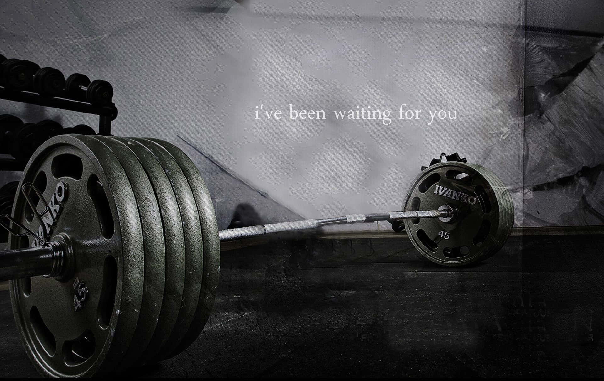 Barbell 桌布 壁紙 — 一個沉重的槓鈴連同槓片放在昏暗的健身房地板上，在戲劇性的燈光下，附有文字「我一直在等你」。