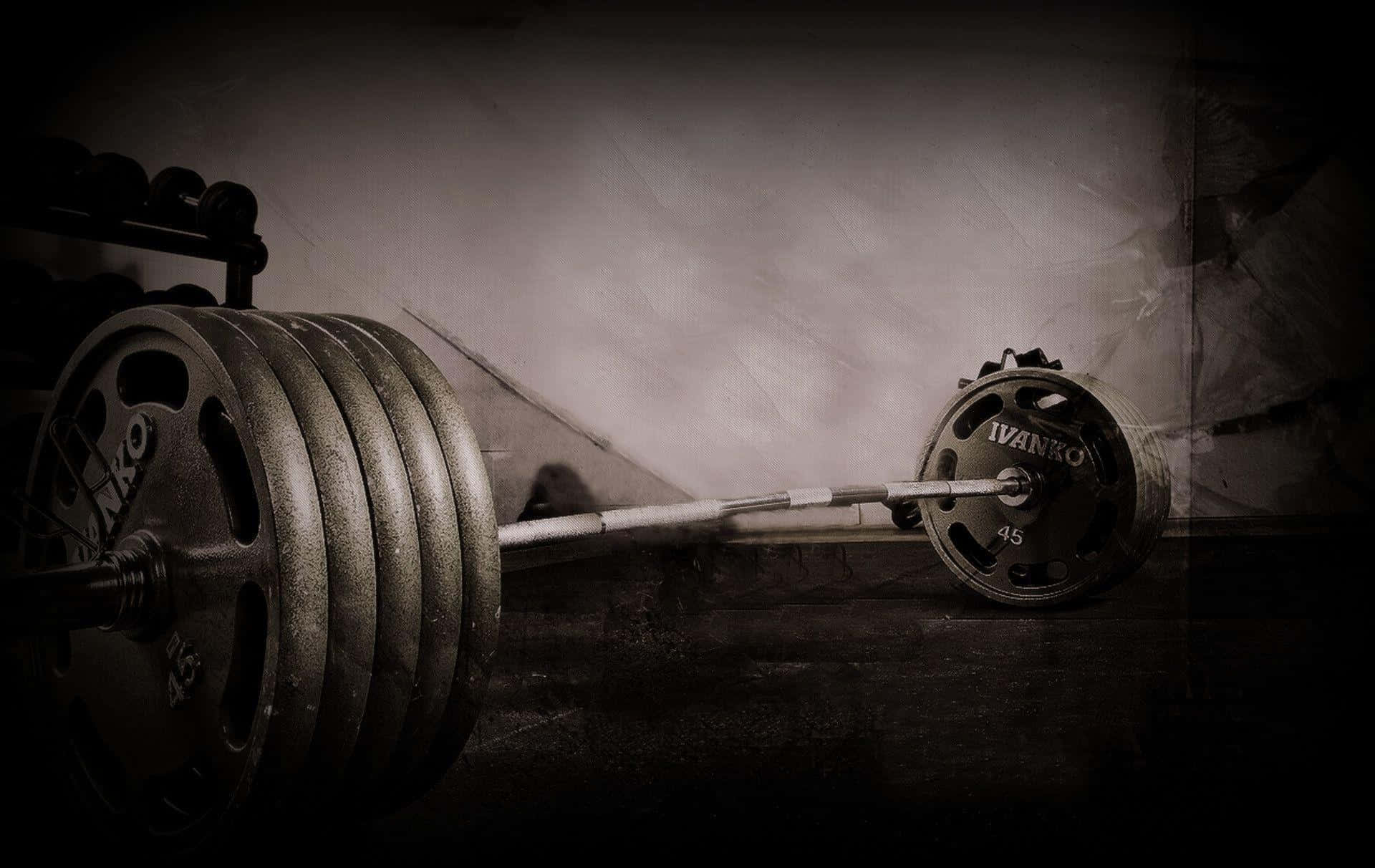 Exercise 桌布 壁紙 — 一個沉重的槓鈴連同疊放的槓鈴片，在戲劇性昏暗燈光下放置在深色健身房地板上。