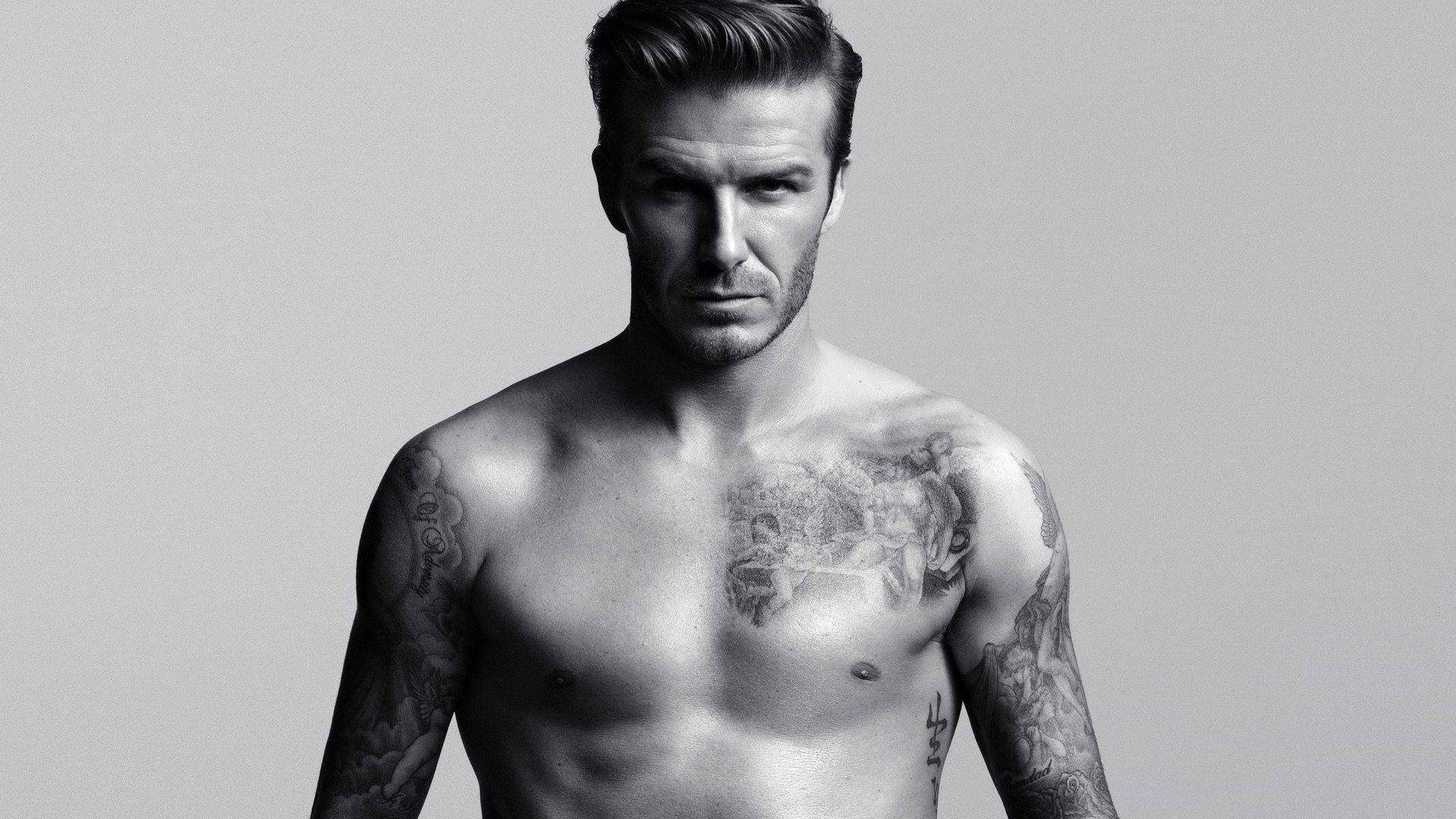 David Beckham 桌布 壁紙 — 一個沒穿上衣的男人，身上有刺青，在純灰色背景前，以高對比度黑白肖像照中，眼神銳利。