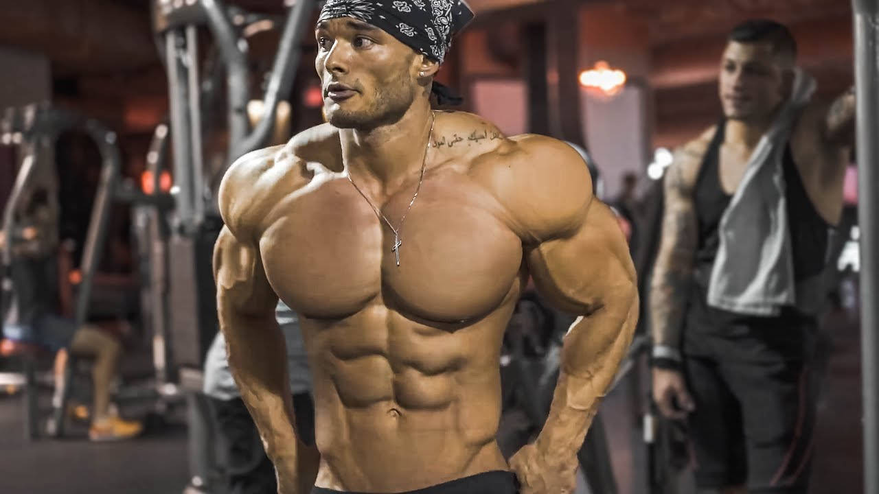 Exercise 桌布 壁紙 — 一個沒穿上衣的肌肉男，戴著頭巾和項鍊，自信地站在健身房，展現出清晰的腹肌和隆起的二頭肌。