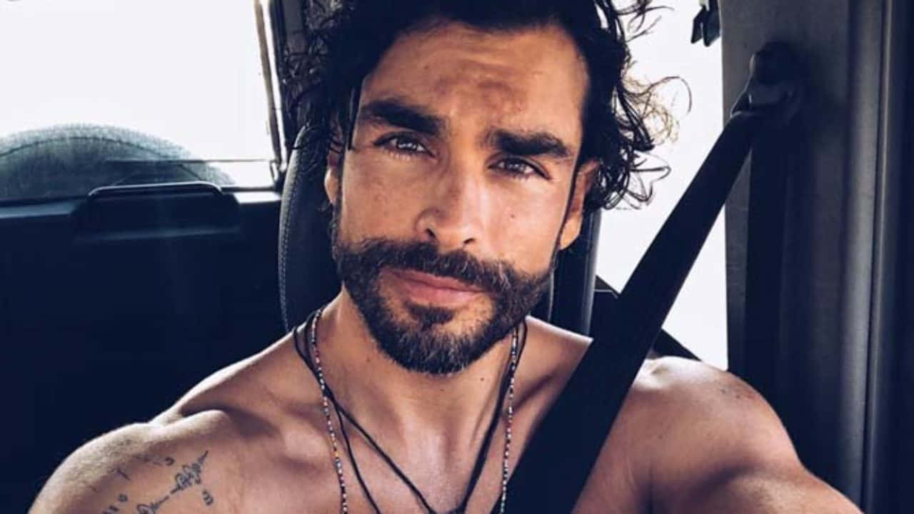 Celebrity 桌布 壁紙 — 一個沒穿衣服、有鬍鬚和紋身的男人，在陽光穿過車窗的車內自信地凝視著。