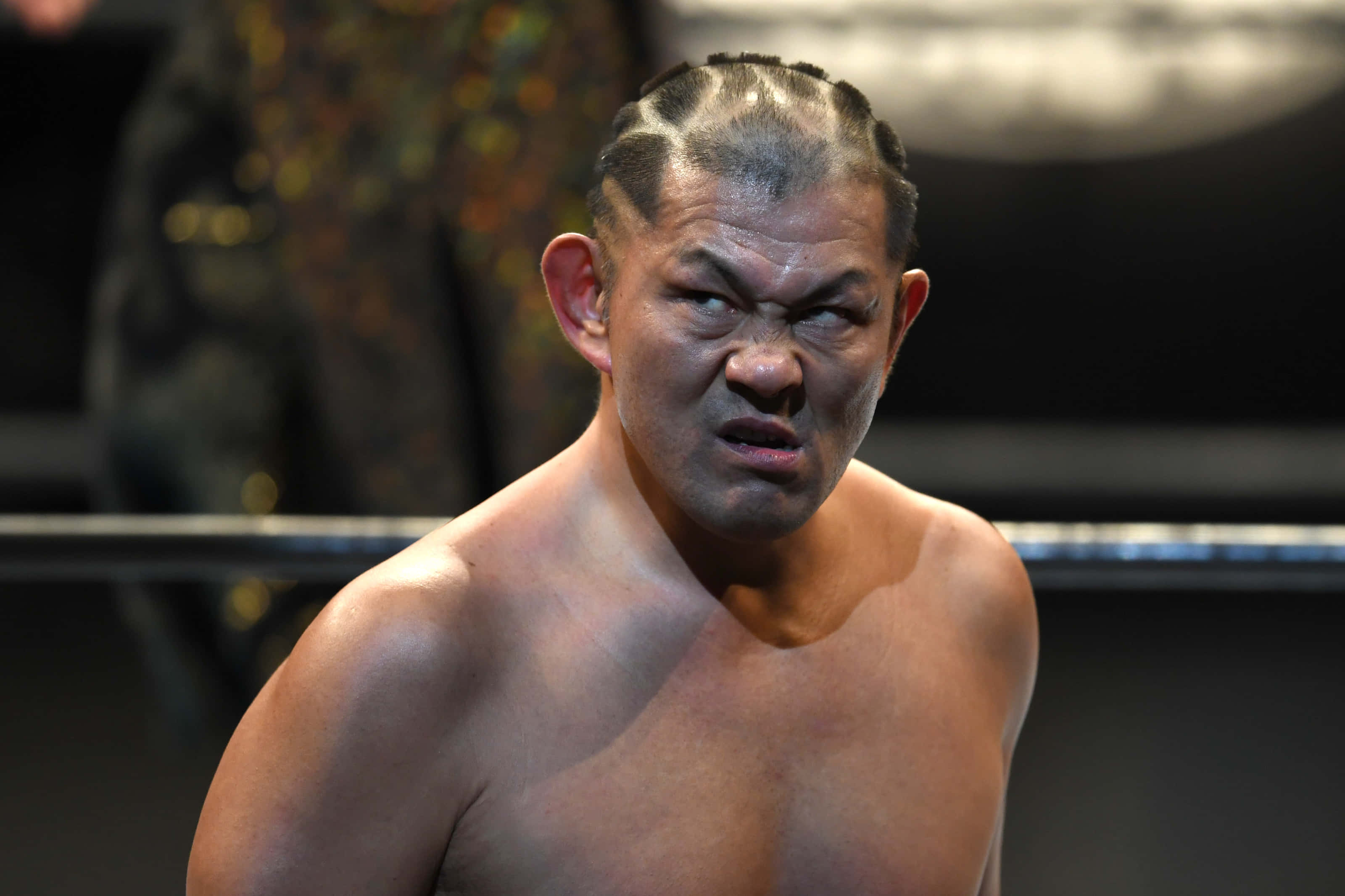 Aew 桌布 壁紙 — 一個沒穿衣服、綁辮子的摔角手在明亮燈光下的擂台上激烈地扭曲表情。