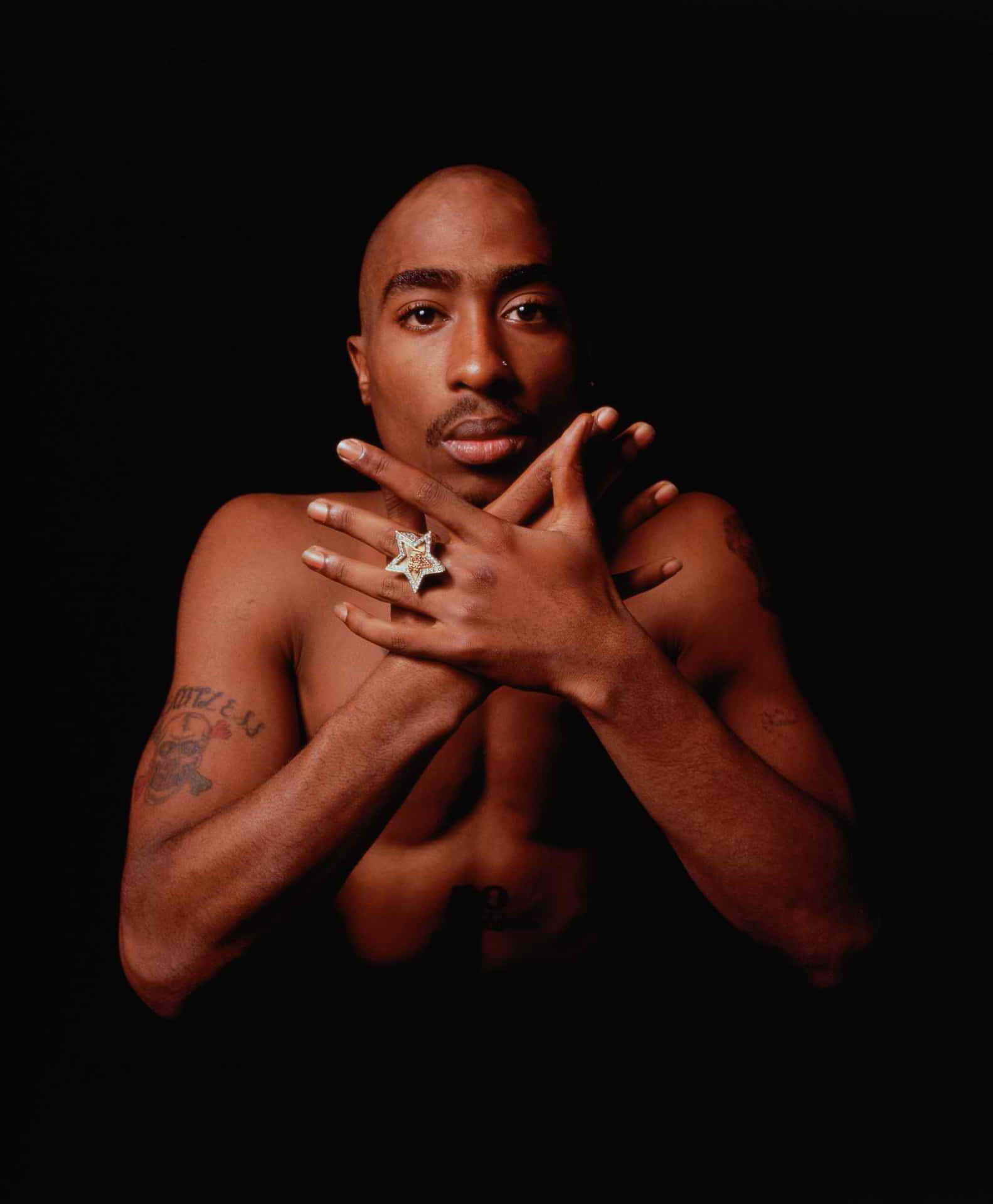 tupac 桌布 壁紙 — 一個沒穿衣服的男人有刺青，在黑色背景前擺姿勢，戴著一個大星星形狀的戒指。