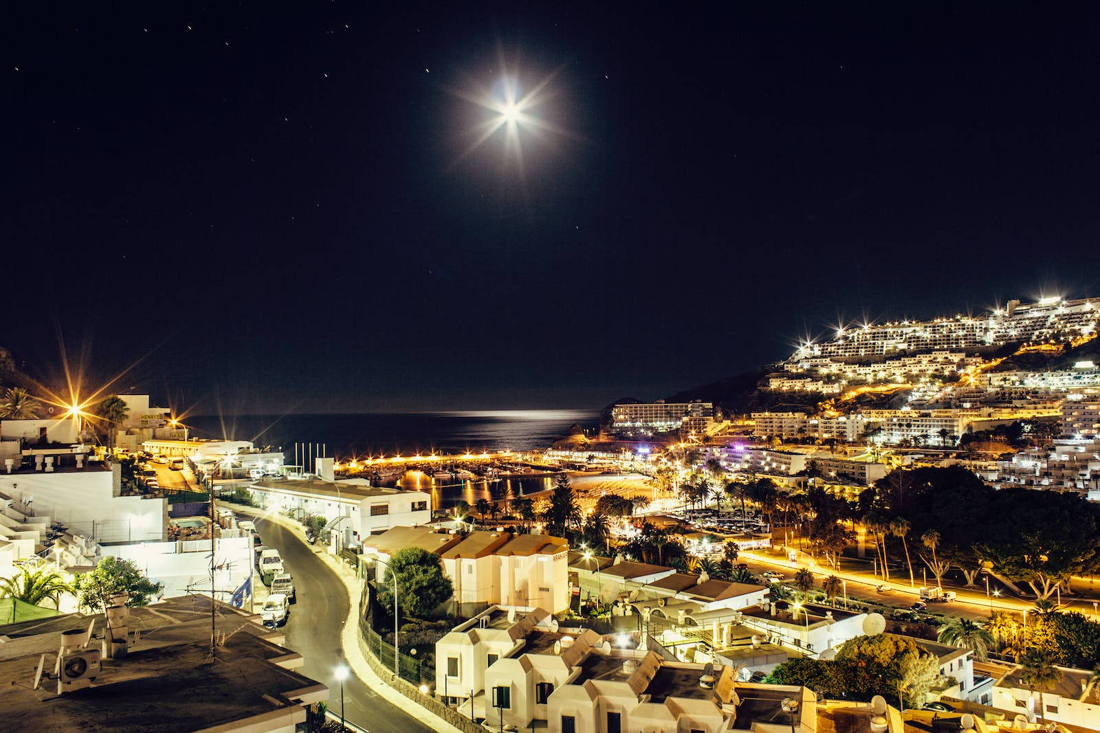 月光 桌布 壁紙 — 一個沿海小鎮在明亮的星空下閃耀的迷人夜景，月光在海面上反射。
