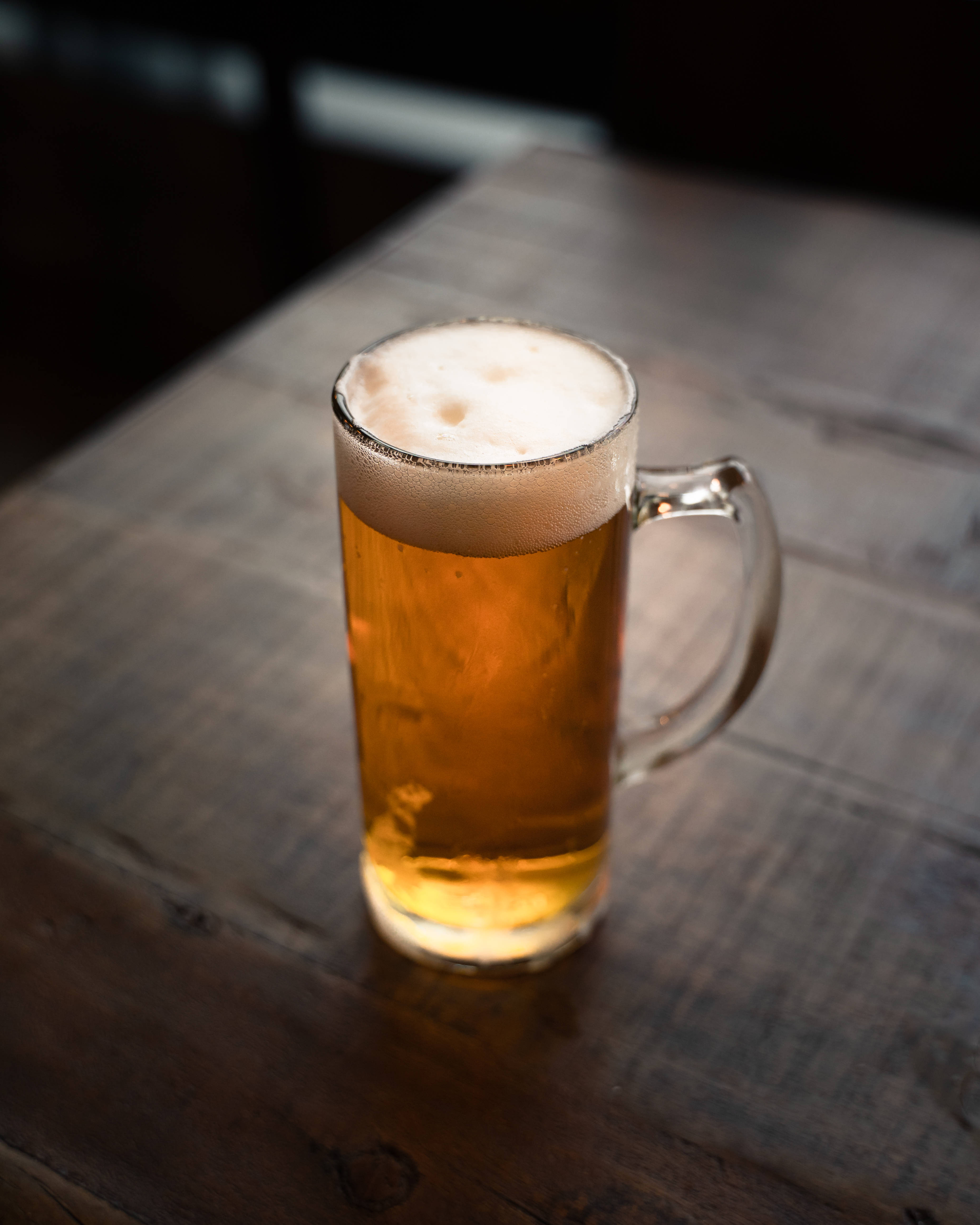 Beer 桌布 壁紙 — 一個泡沫豐富的金色啤酒杯放在質樸的木桌上，溫暖的環境燈光下。