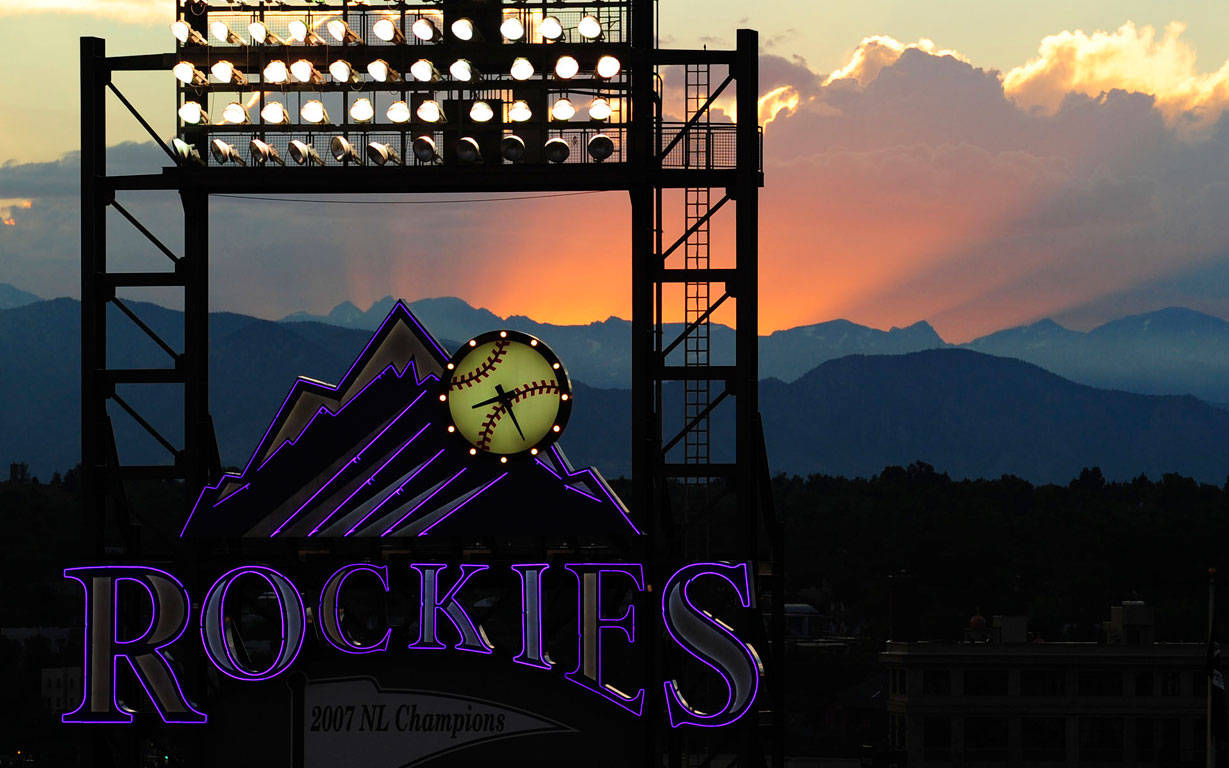 Rockies 桌布 壁紙 — 一個洛磯隊棒球霓虹標誌在戲劇性的日落和山脈剪影中發光。